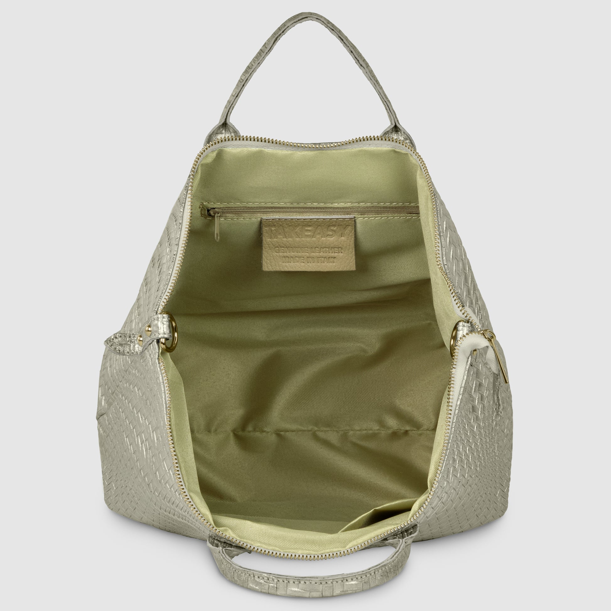 A light beige, textured handcrafted designer bag stands open, revealing its spacious, pale green interior with a zippered pocket and a visible rectangular label stitched on the inside.