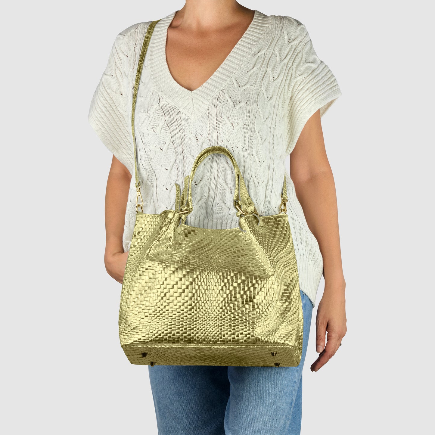 A person wearing a white knit short-sleeve sweater and blue jeans holds a large, handcrafted women's bag with both handles and a shoulder strap against a plain light gray background.