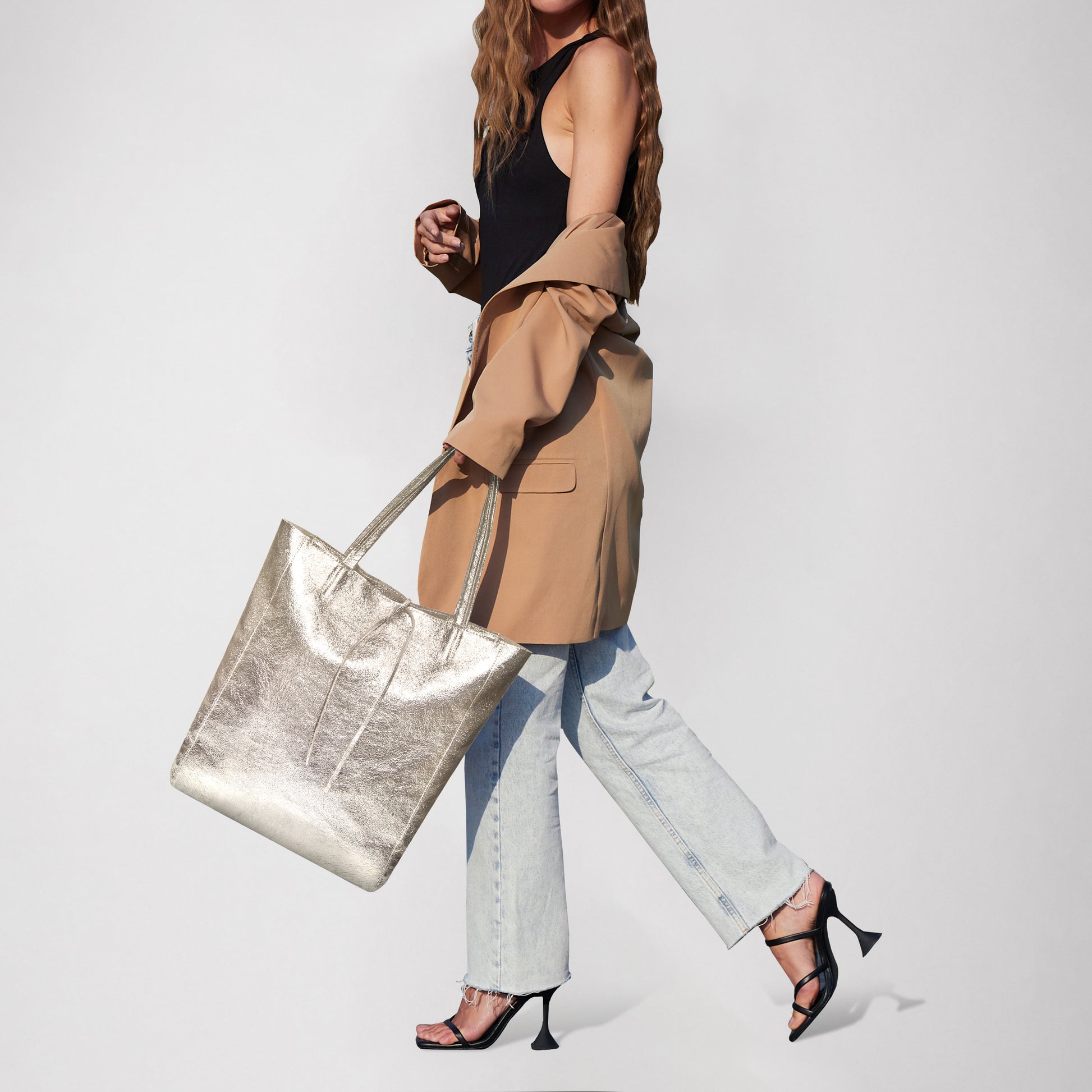 Woman walks in stylish outfit with a metallic tote bag and high heels.