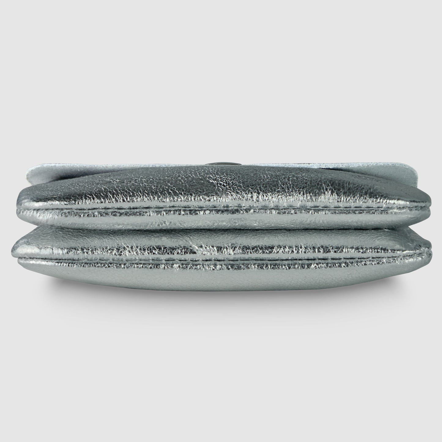A metallic silver Gleam Suede Leather clutch purse is shown lying flat, viewed from the side, with a soft, textured surface and a fold-over design that reflects quiet luxury against a plain light background.