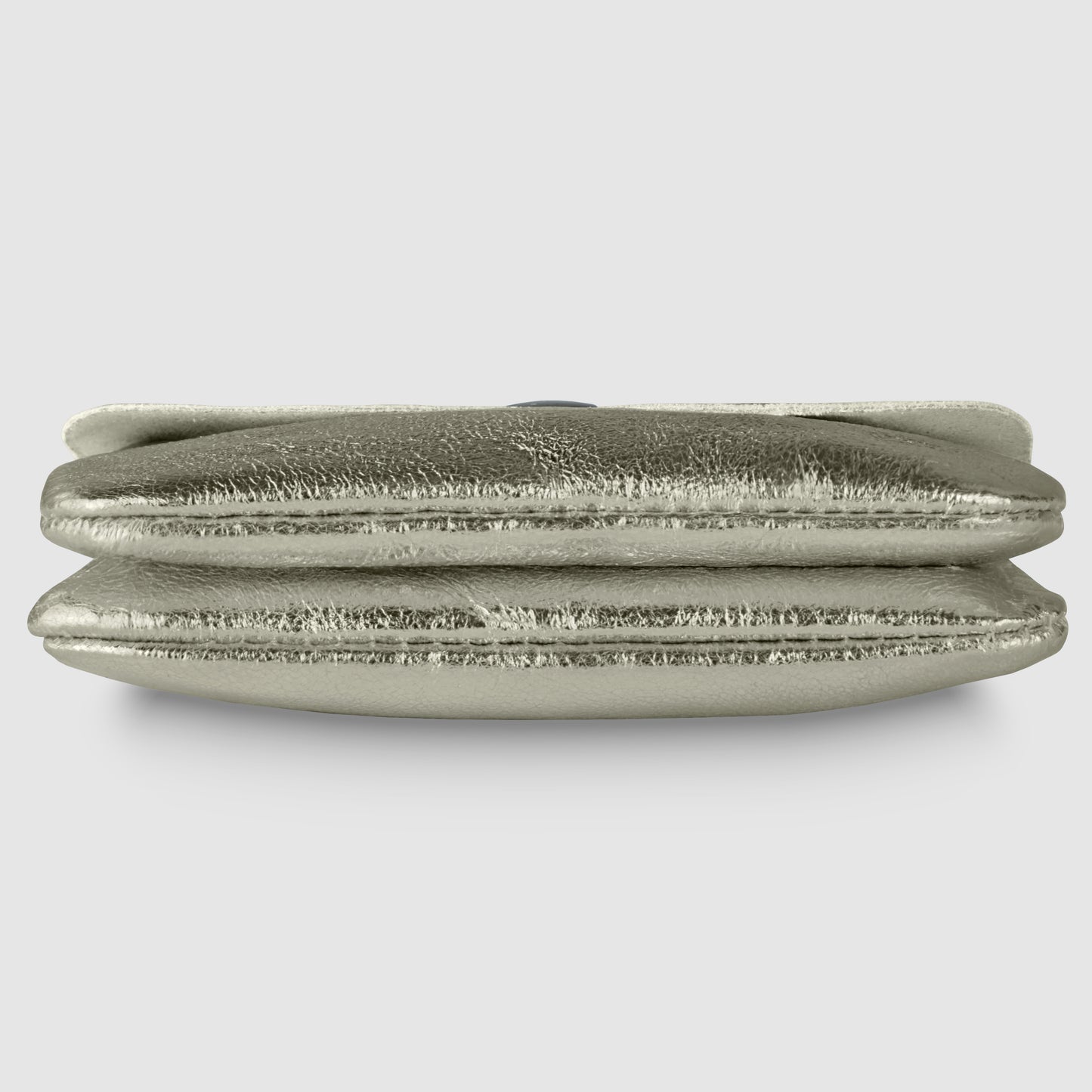 A metallic silver clutch bag with a slightly wrinkled, shiny texture, viewed from the side against a plain light gray background, exuding quiet luxury reminiscent of a refined Italian wallet.