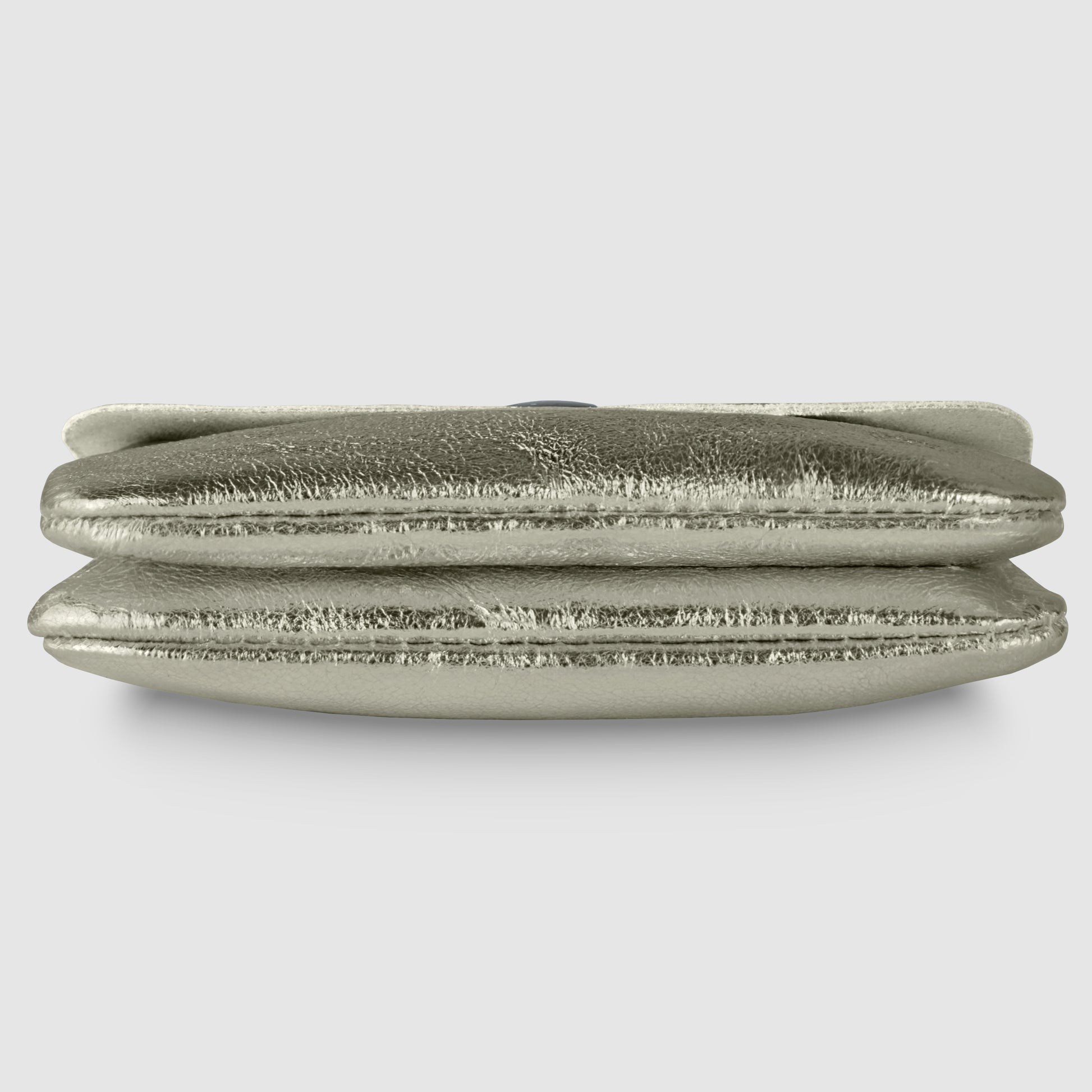 A metallic silver clutch bag with a slightly wrinkled, shiny texture, viewed from the side against a plain light gray background, exuding quiet luxury reminiscent of a refined Italian wallet.
