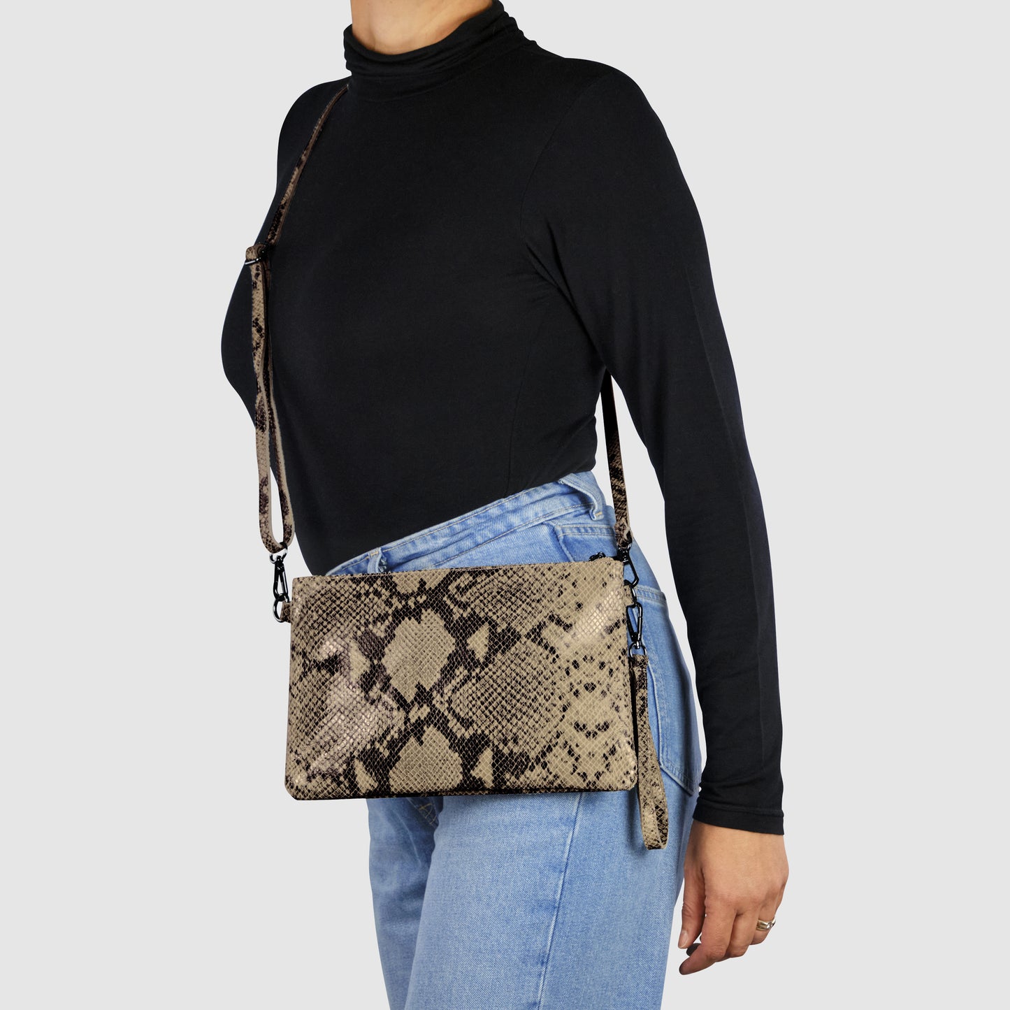 A person wearing a black turtleneck and light blue jeans carries an Italian handcrafted python suede bag with a matching strap, styled crossbody against a plain light background.