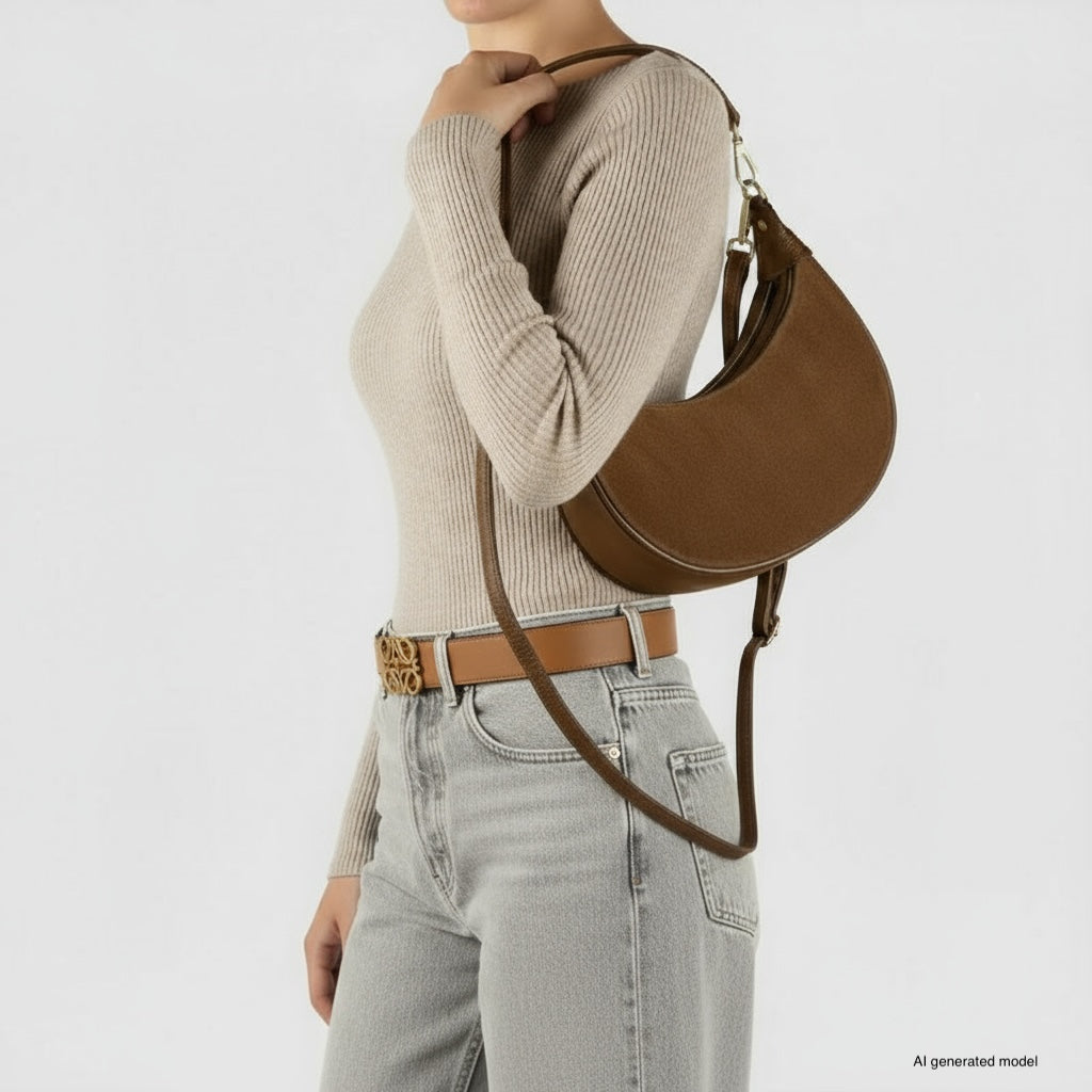 A woman wearing a beige ribbed sweater and light gray jeans carries an Italian leather bag. Her belt is tan with a decorative buckle. She is shown from the shoulders down against a plain background.