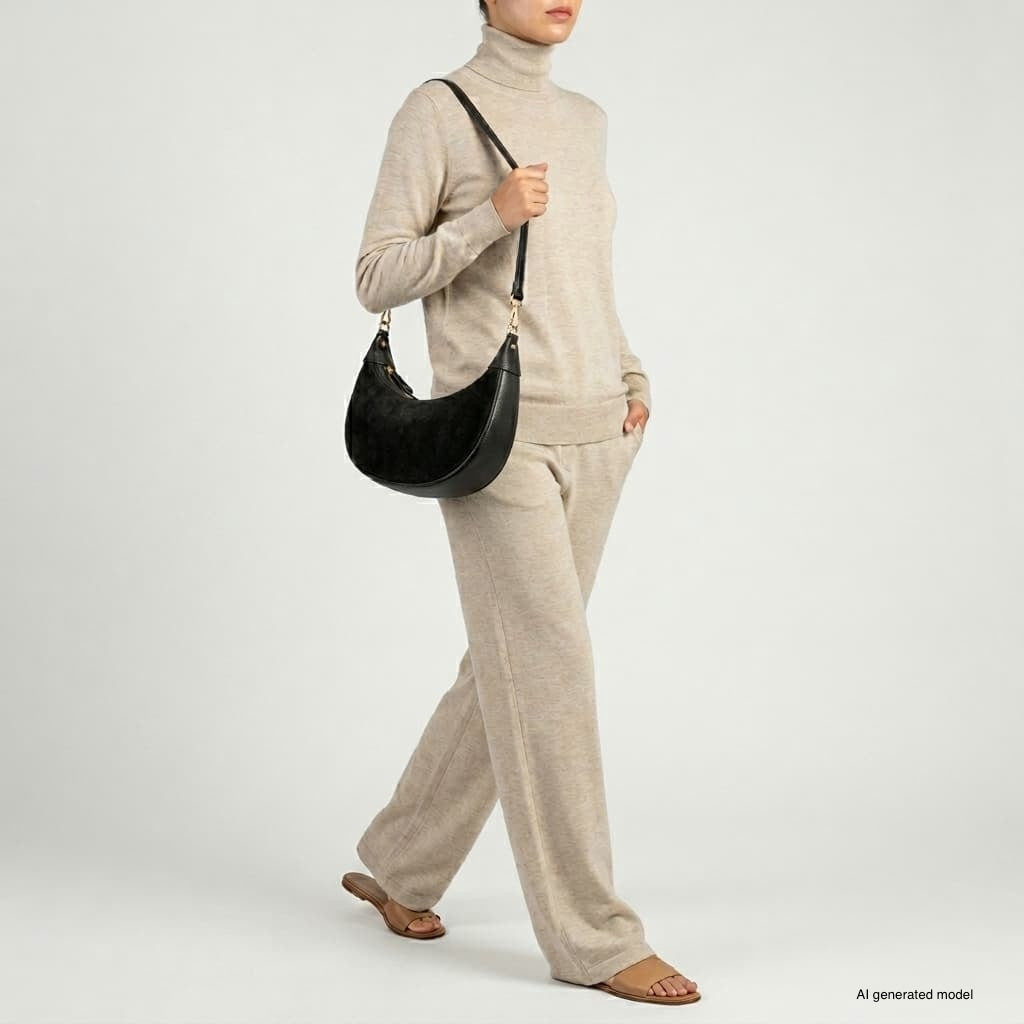 A person wearing a beige turtleneck sweater and matching pants walks while carrying a sleek Italian leather bag. They are wearing sandals, with one hand in their pocket. The background is plain light gray.
