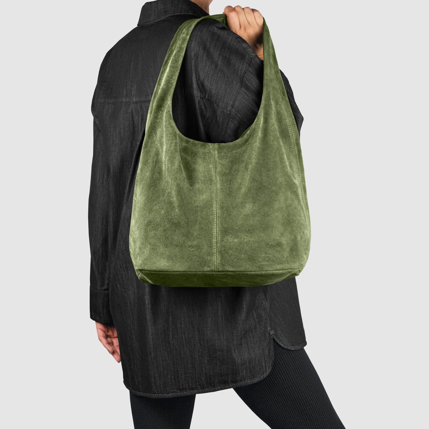 A person wearing a black outfit holds a large, olive-green Italian suede bag against a plain light gray background.