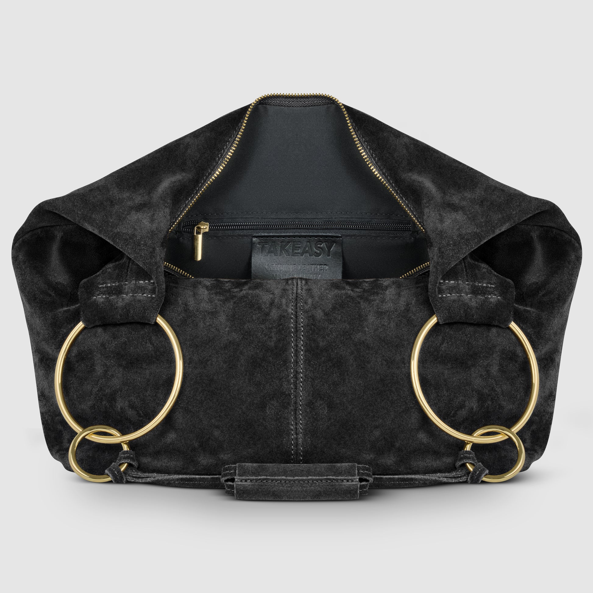 A natural suede bag in black with gold circular handles, an open zipper revealing an inner pocket, and the word TAKEASY on a tag inside. The background is light gray.