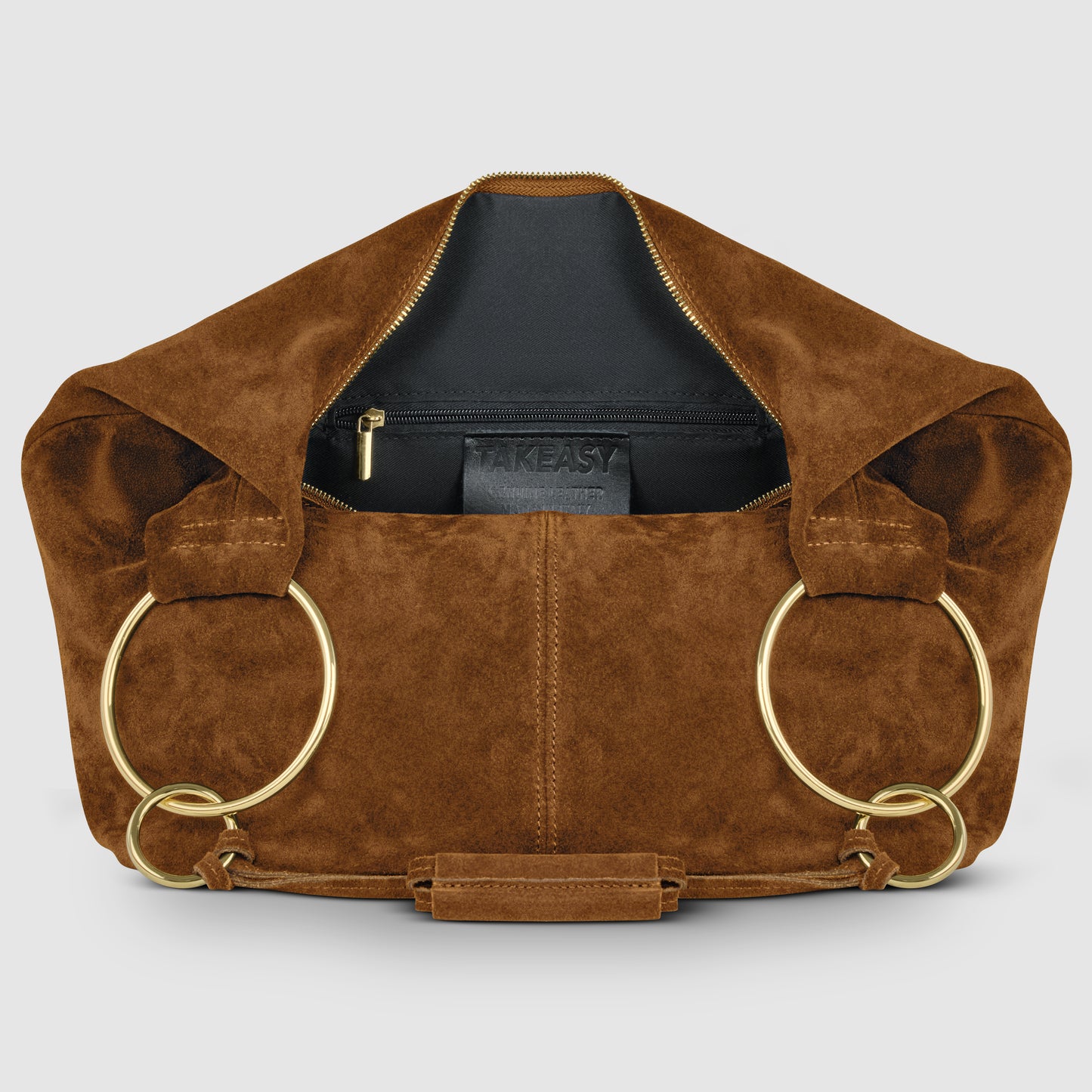 A brown natural suede handbag with large gold rings as handles is open to reveal a black interior, zippered pocket, and a visible "TAKEASY" label inside.