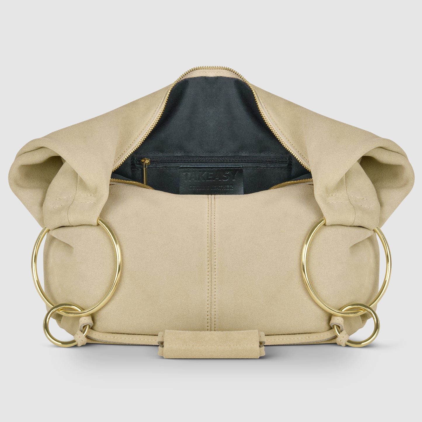 A beige natural suede handbag with large gold metal rings on both sides, displayed open to show a black interior lining and a zippered pocket—an elegant Italian handmade bag crafted with care.