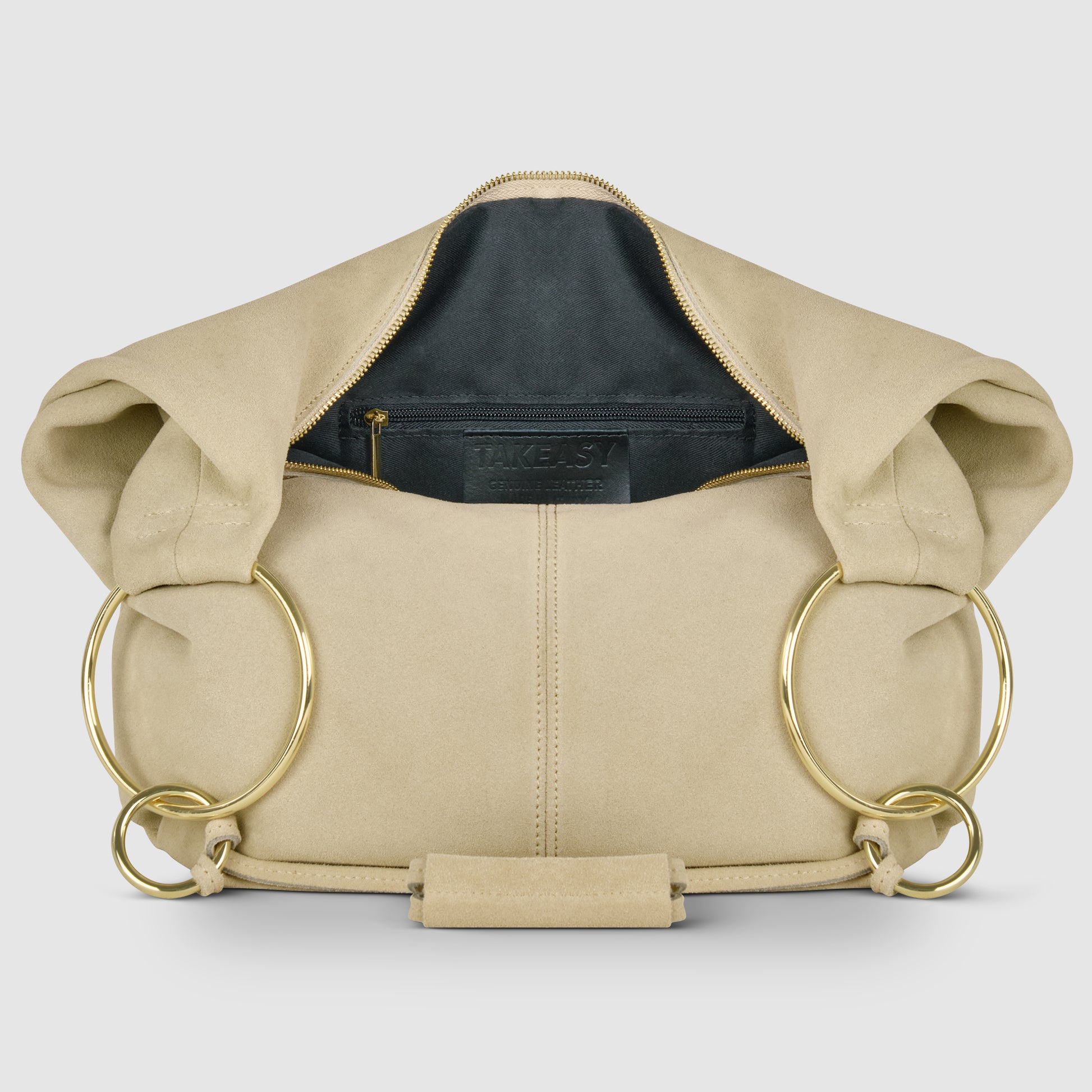 A beige natural suede handbag with large gold metal rings on both sides, displayed open to show a black interior lining and a zippered pocket—an elegant Italian handmade bag crafted with care.