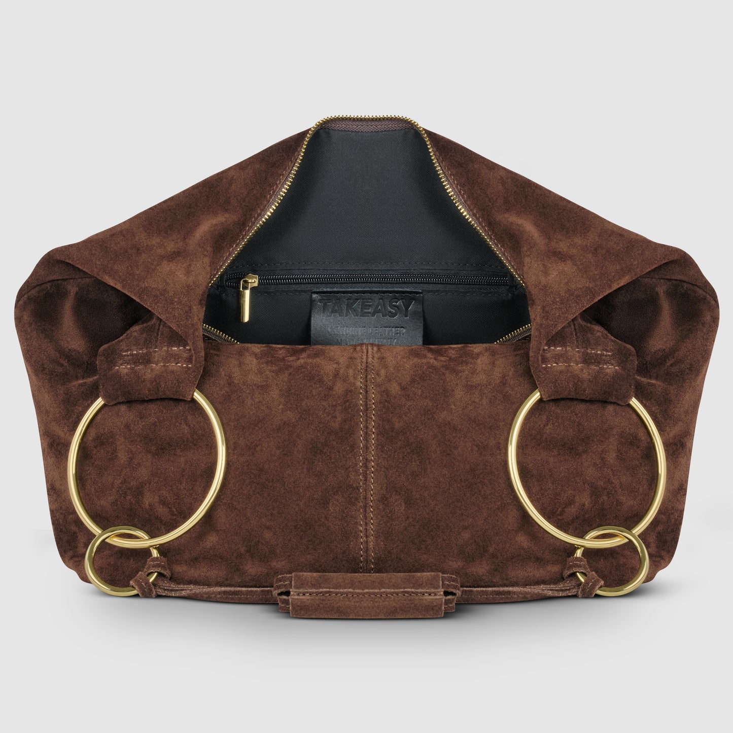A natural suede bag with a zipper opening, large gold metal rings as handles, and a black inner pocket labeled TAKEASY. This Italian handmade bag is displayed against a plain light background.