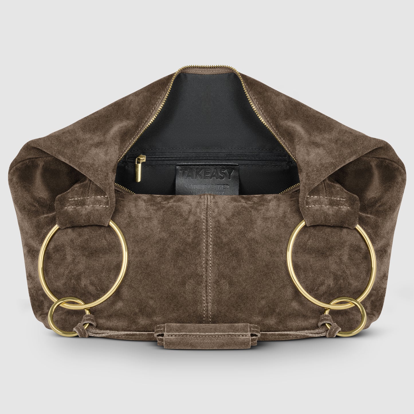 A brown suede leather bag with large gold rings as handles, a gold zipper partially open to reveal a black interior pocket labeled TAKEASY, showcases Florentine craftsmanship against a plain light gray background.