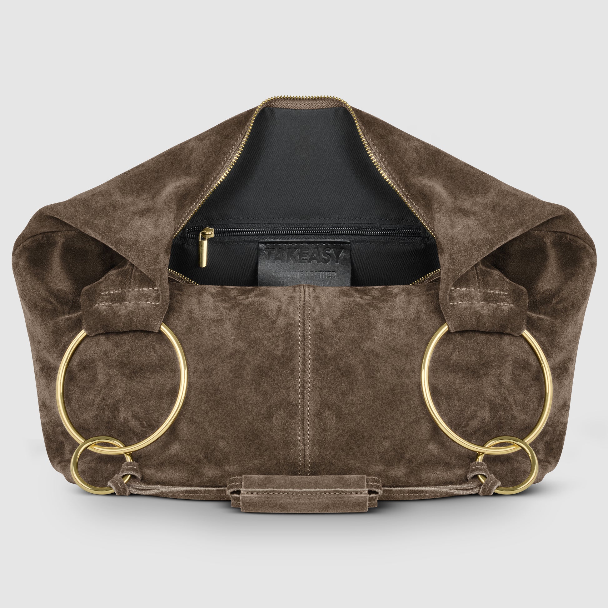 A brown suede leather bag with large gold rings as handles, a gold zipper partially open to reveal a black interior pocket labeled TAKEASY, showcases Florentine craftsmanship against a plain light gray background.