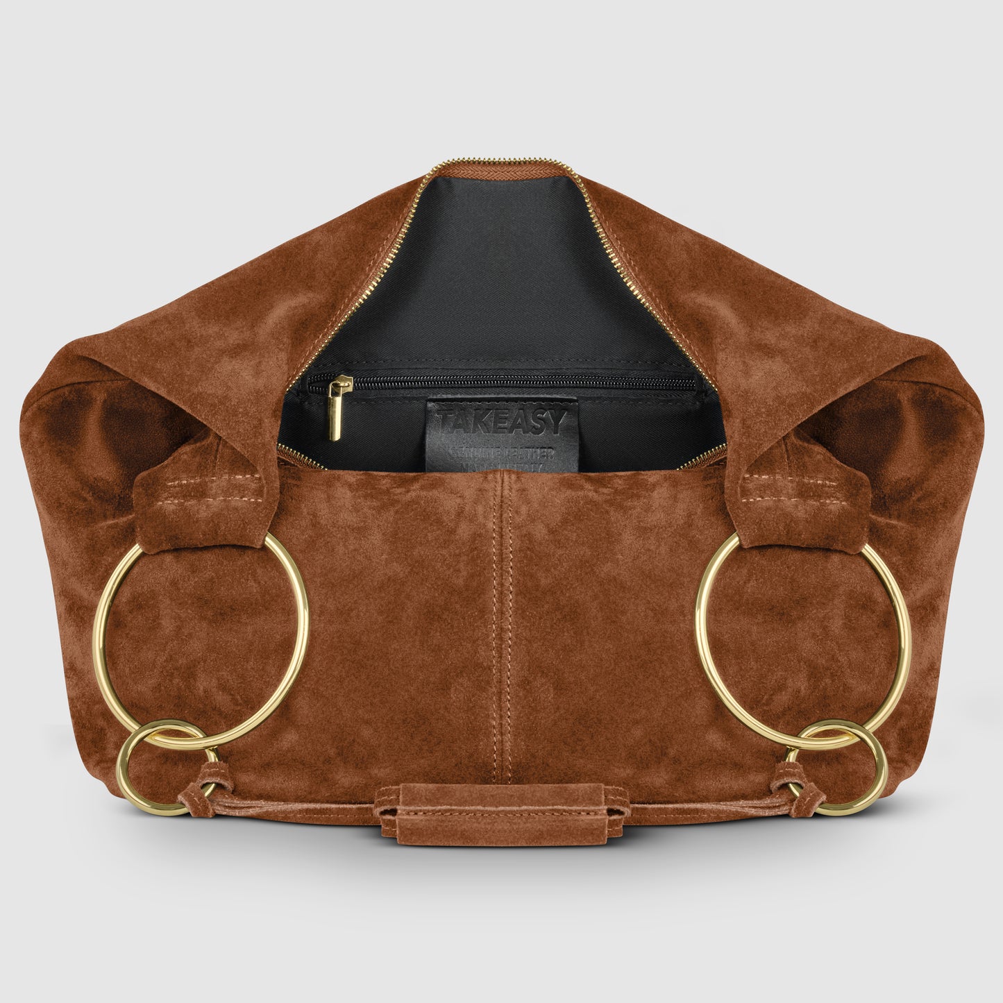 A brown natural suede handbag with large gold rings for handles, an open top revealing a black inner pouch with a zipper, and a TAKEASY label inside—an elegant Italian handmade bag.