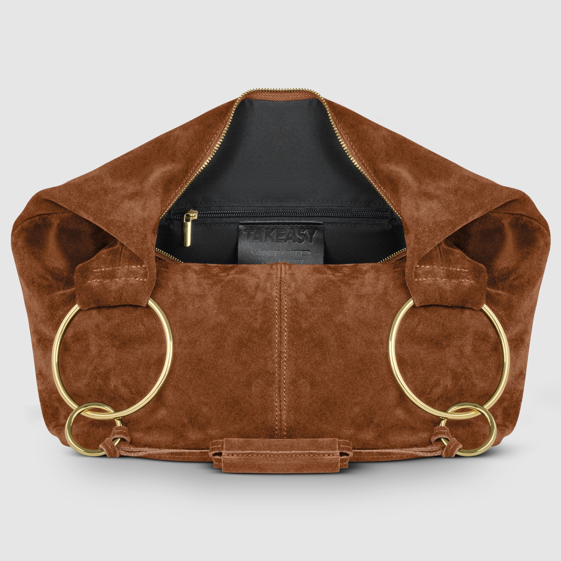 A brown natural suede handbag with large gold rings for handles, an open top revealing a black inner pouch with a zipper, and a TAKEASY label inside—an elegant Italian handmade bag.
