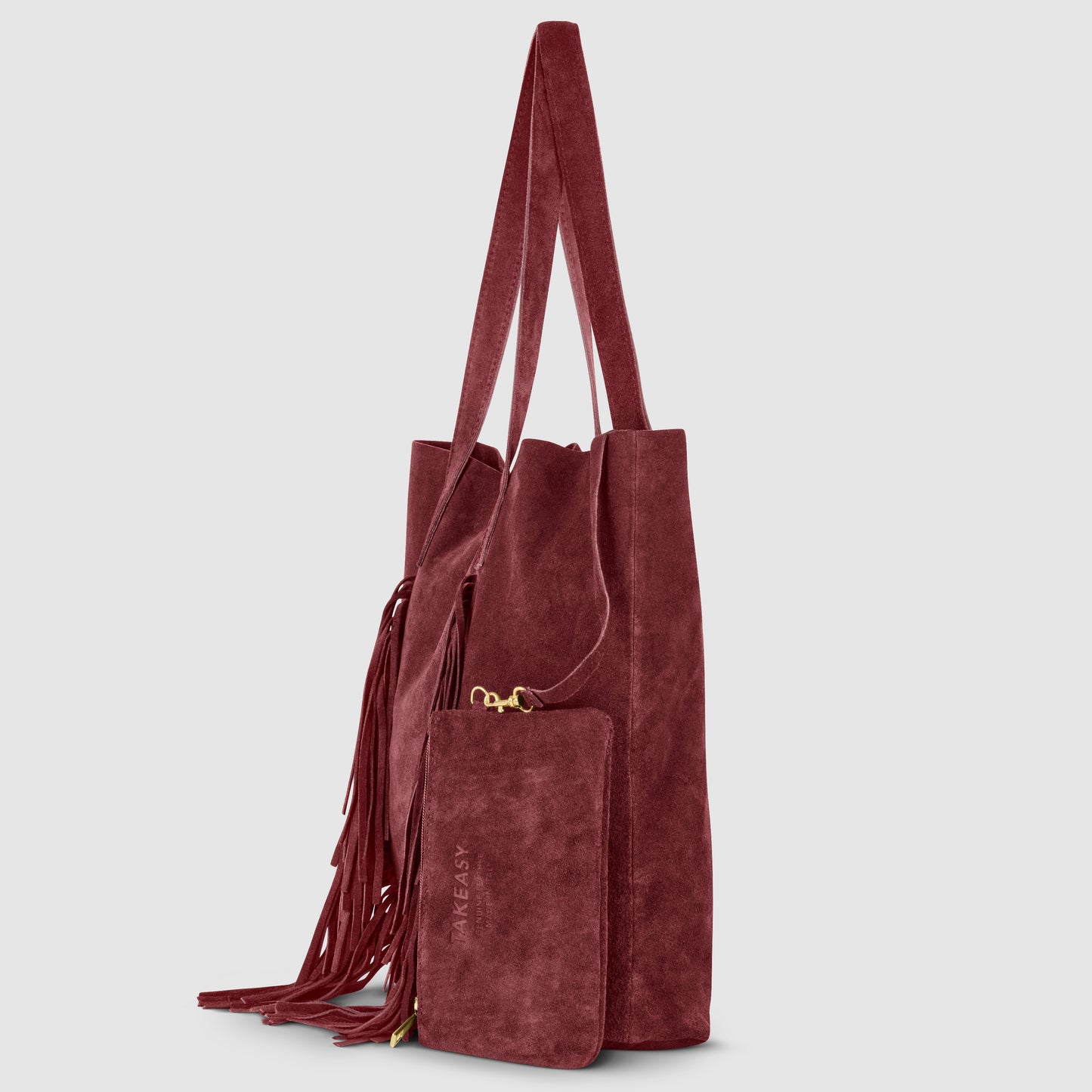 A bohemian handbag in burgundy suede with long handles, fringe detailing, and a matching detachable zippered pouch, this handmade Italian bag is shown against a light gray background.