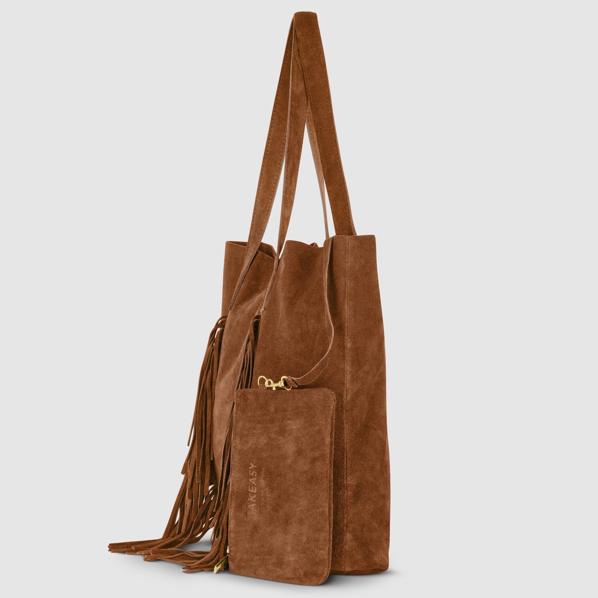 A brown suede handbag with long handles, a matching suede pouch attached by a gold zipper, and decorative fringe detail on the side creates a chic bohemian handbag look, shown against a light gray background.
