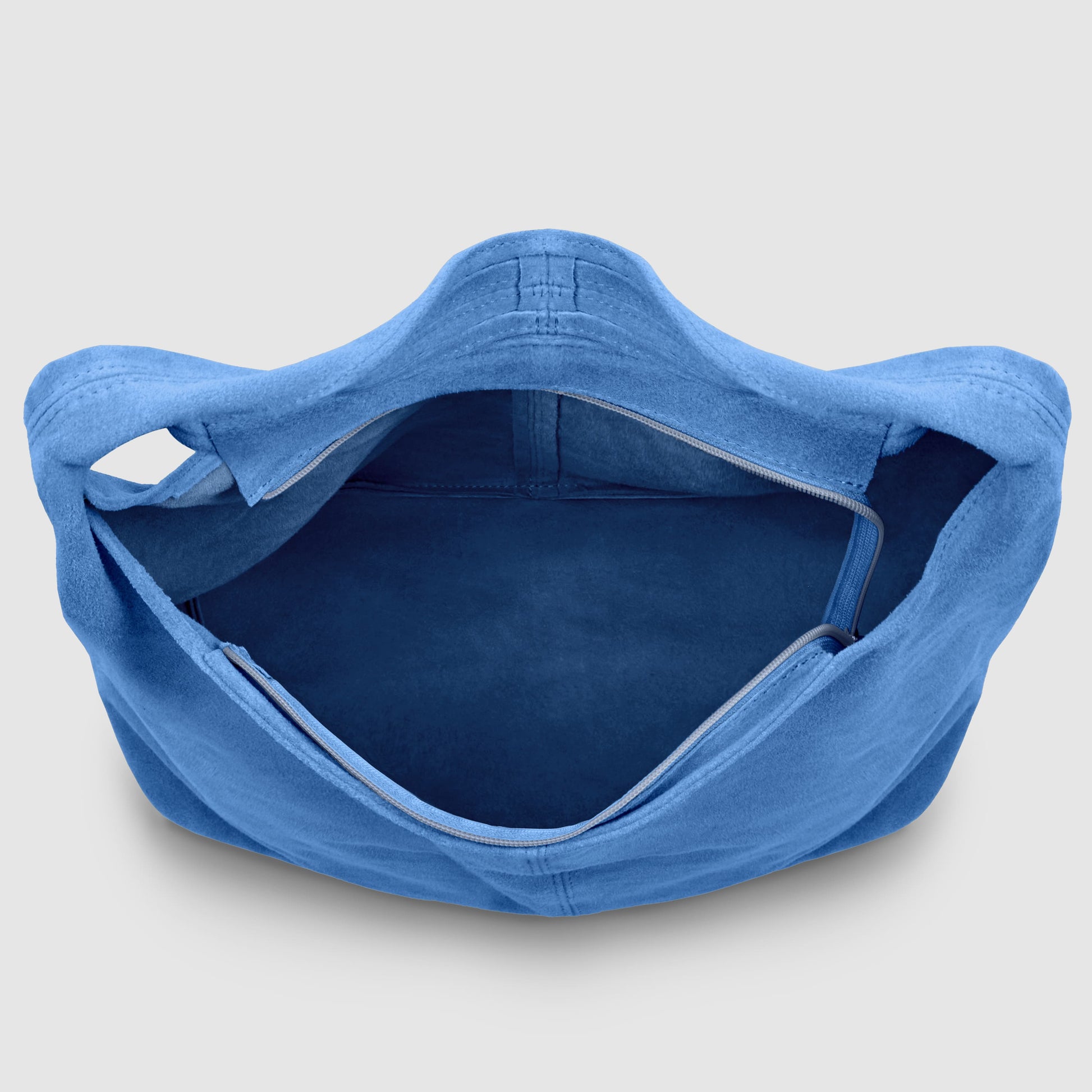 A top-down view of an Italian handcrafted bag in open blue suede, featuring a wide main compartment and an interior zippered pocket, displayed on a light gray background.
