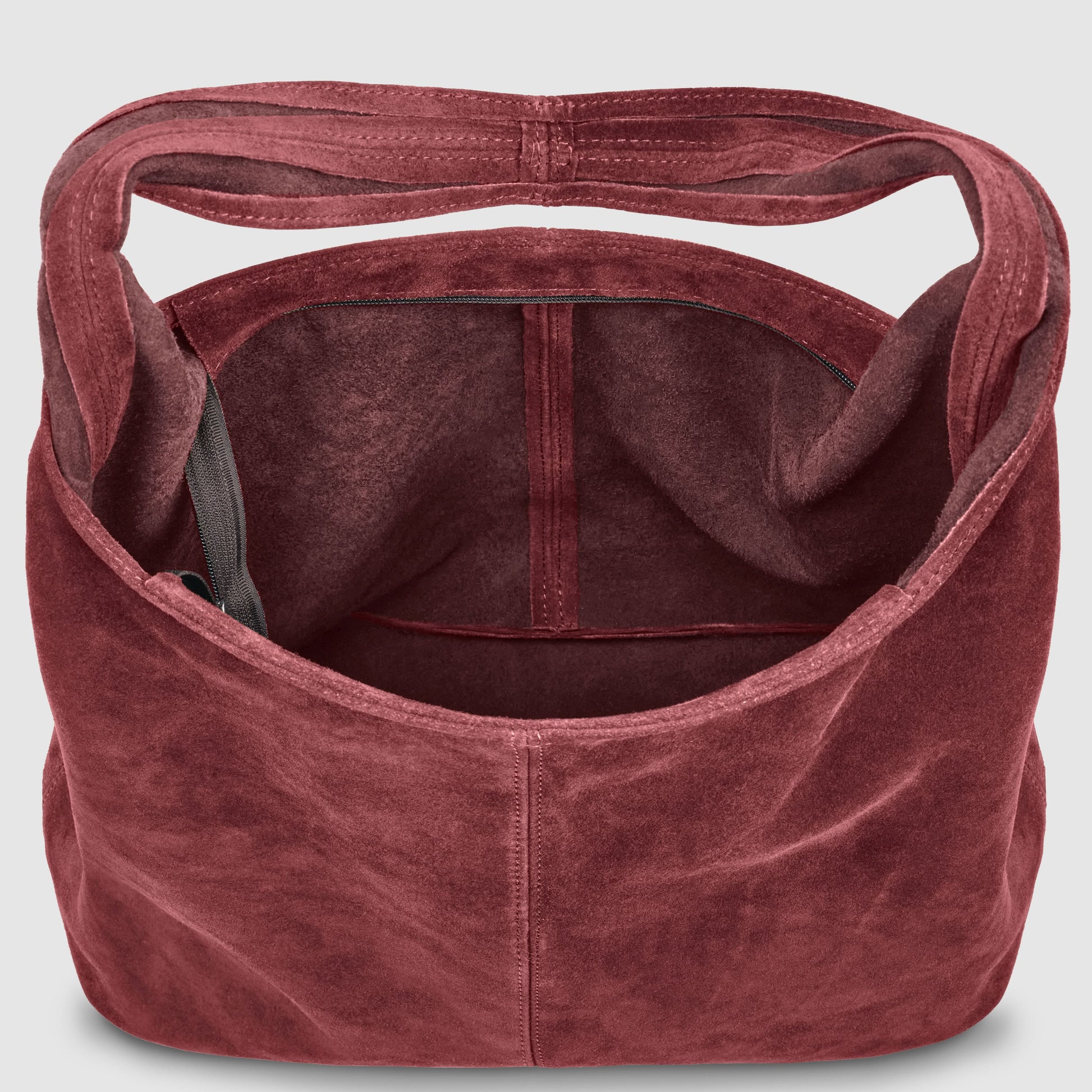 A top-down view of an Italian handcrafted bag in deep burgundy suede, featuring a single wide shoulder strap and a dark inner pocket—an effortlessly slouchy suede shoulder purse with ample room inside.