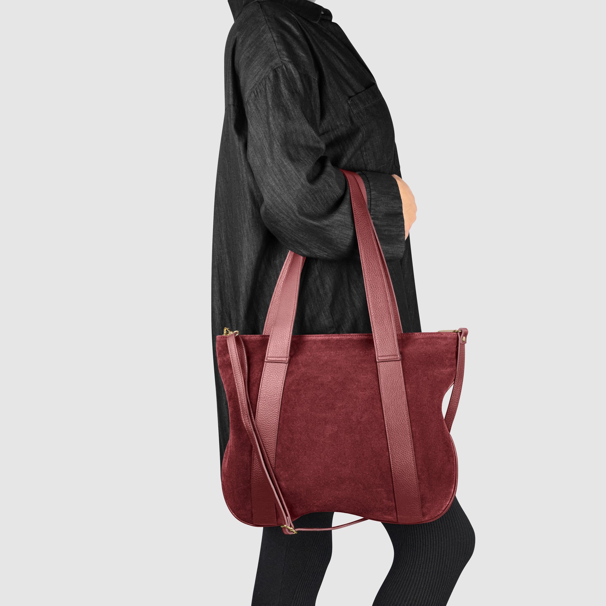 A person in a loose-fitting black outfit carries a large Italian handcrafted bag with double handles over their shoulder, set against a plain light gray background.