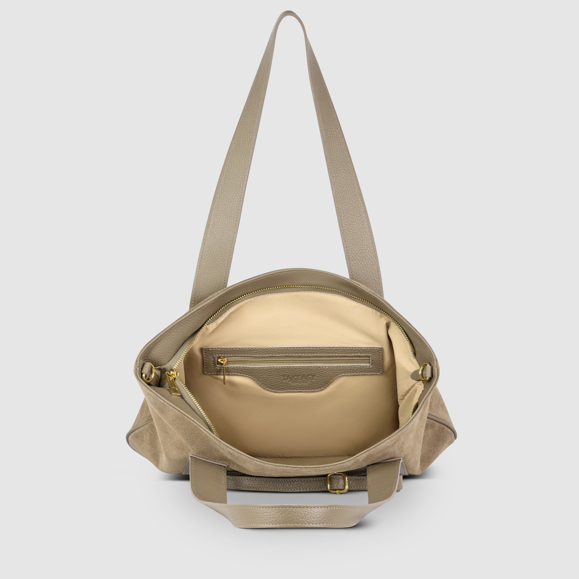 A taupe Italian leather bag with a wide strap is shown open, revealing a beige interior with a zippered pocket and gold zipper pulls. The outer texture blends suede and leather, reflecting classic Florentine leather traditions.