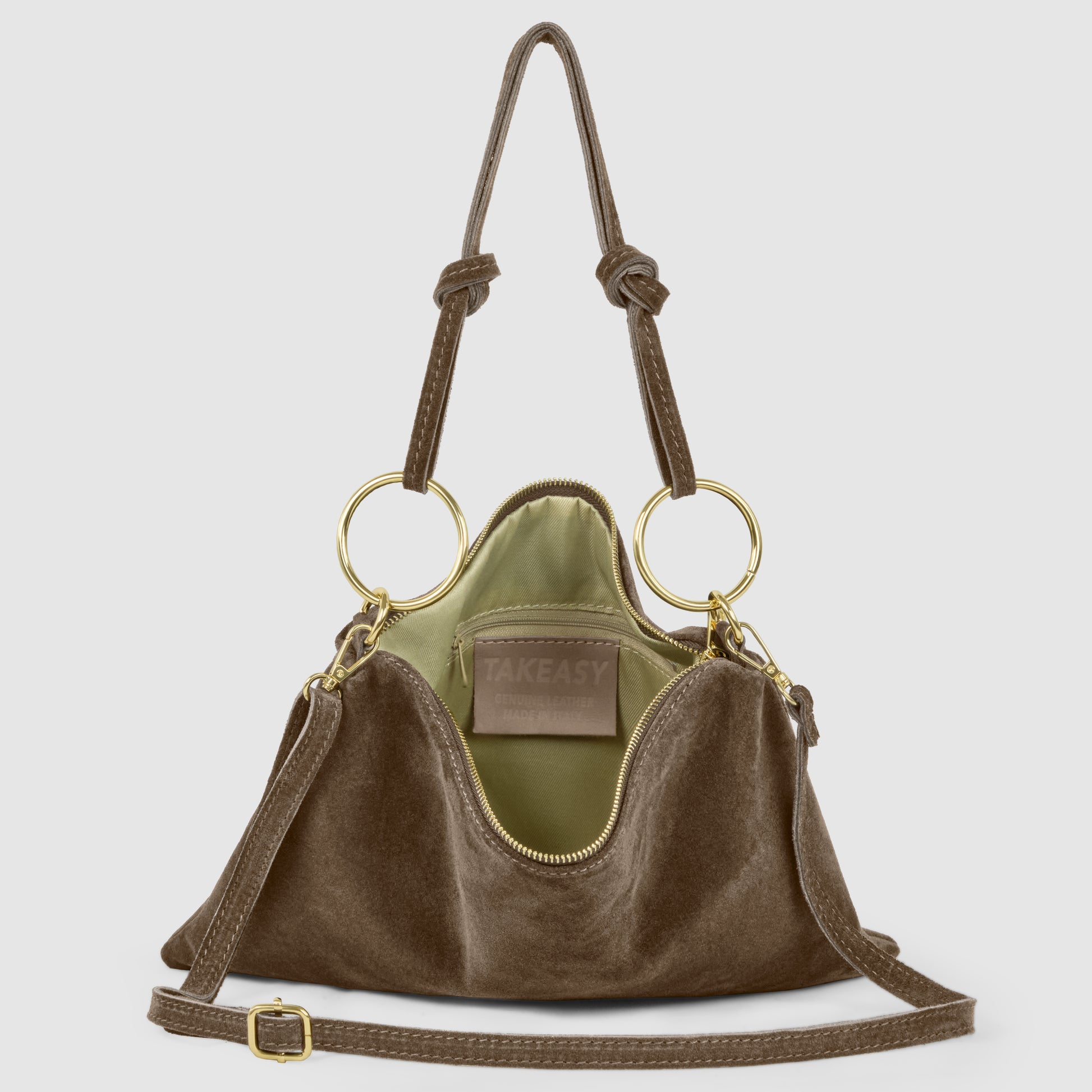 A brown suede leather purse with gold ring handles, tan adjustable shoulder strap, and green interior lining. This Italian handbag is open, revealing a label that reads TAKEASY inside.