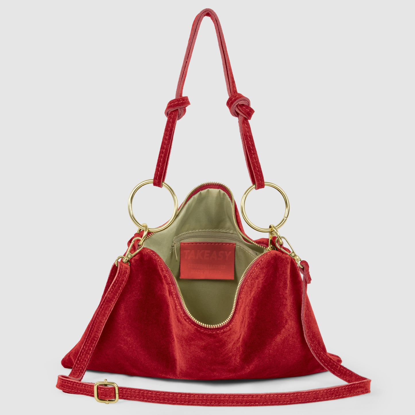 A red velvet Italian suede purse with gold rings, an adjustable strap, and knotted handles. The bag is open, revealing a green interior and a label that reads TAKEASY.