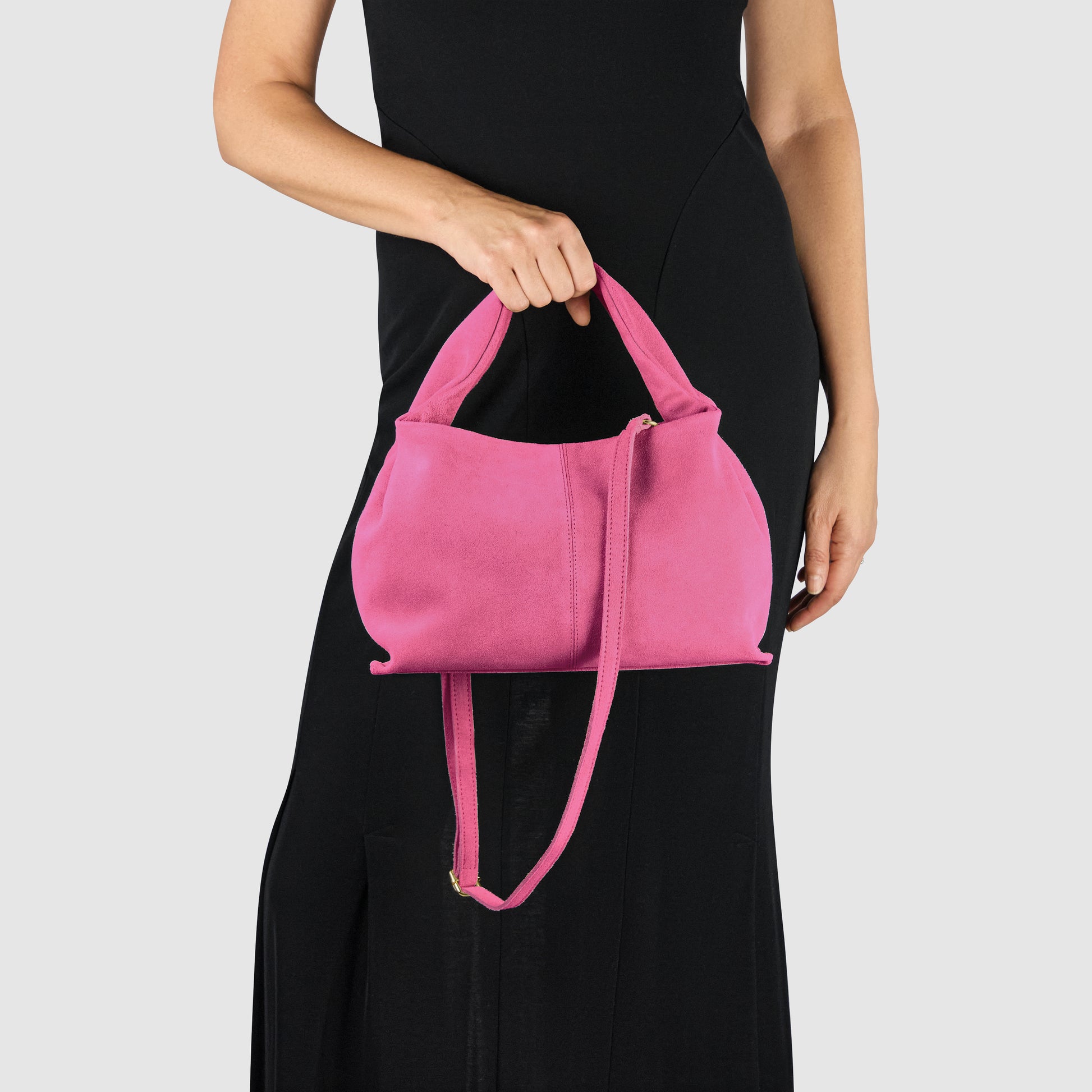 A person wearing a sleeveless black dress holds a sculptural handbag with both a short handle and a long strap against a plain light background.
