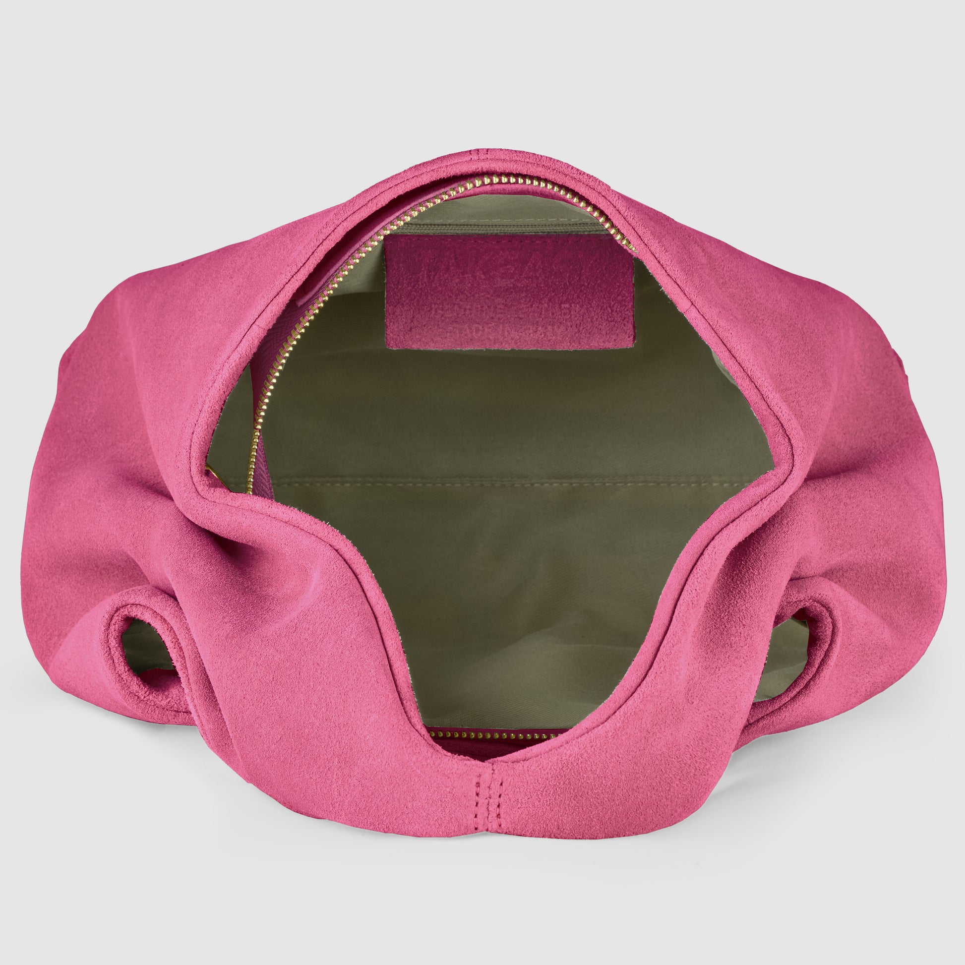 A pink handcrafted suede bag with a gold zipper, shown open to reveal an empty, light gray interior lining. The bag is photographed from above against a plain white background.