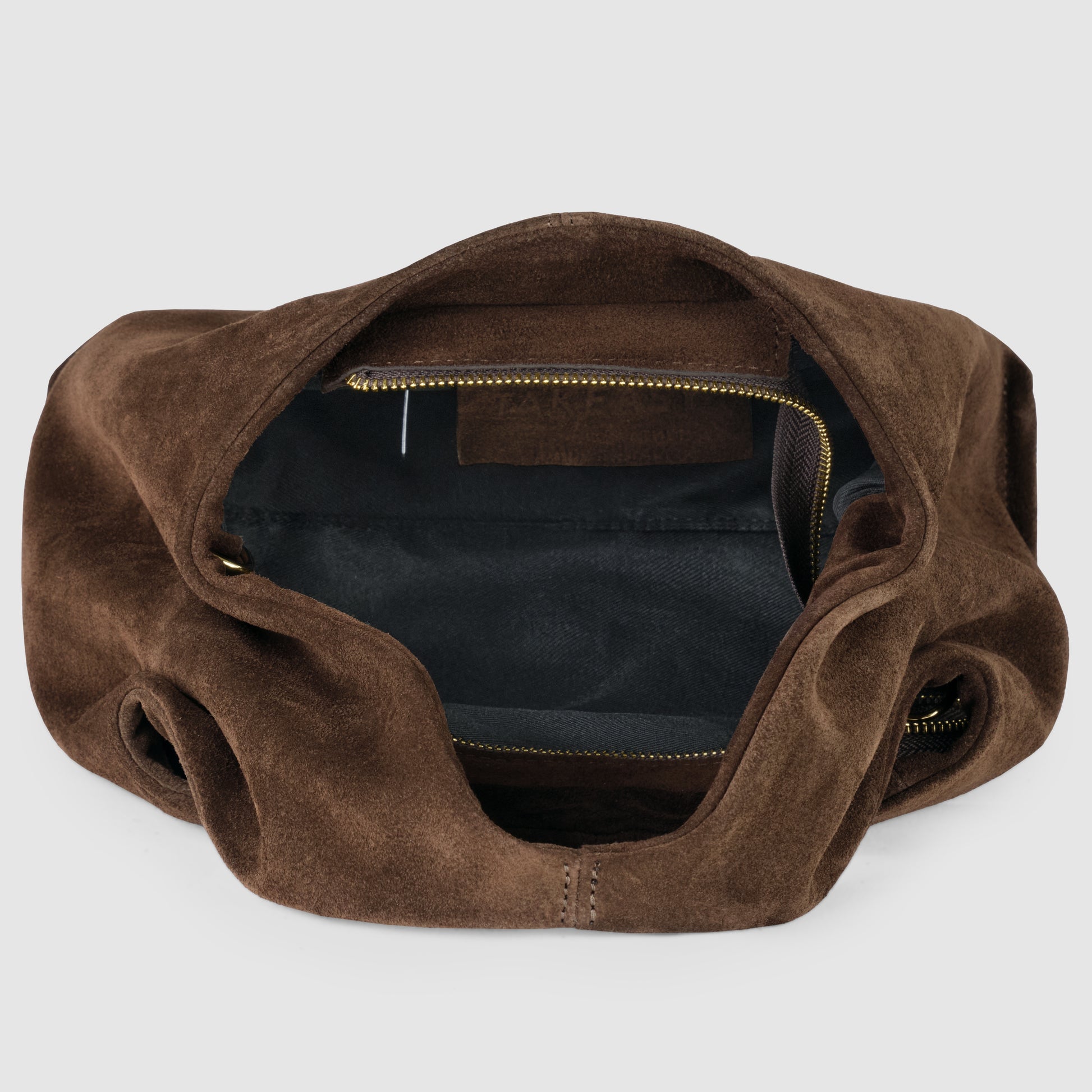 A brown handcrafted suede bag with a zippered inner pocket, shown open and empty, revealing a black fabric lining inside.
