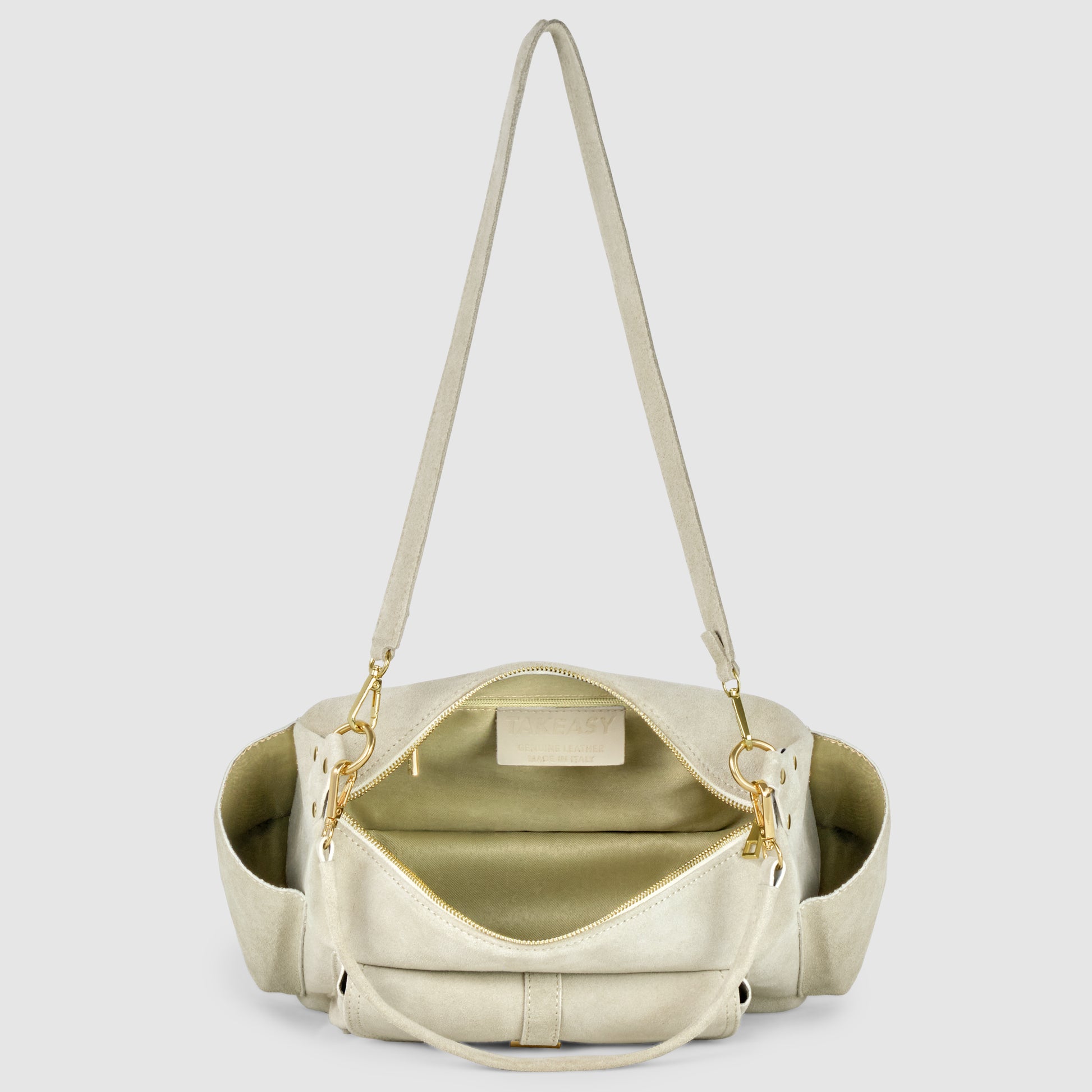 A beige leather shoulder bag, crafted with Florentine leatherworking, is shown open to reveal a spacious, light-colored interior with a zippered pocket. The bag features gold hardware, an adjustable strap, and convenient side pockets.