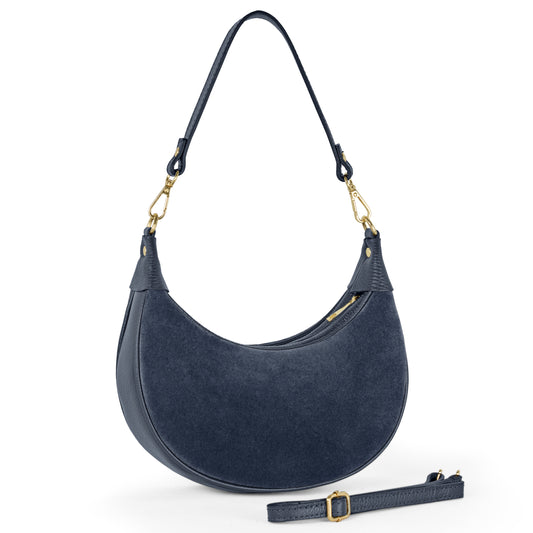 A crescent-shaped navy blue suede leather bag with gold hardware, a short handle, and an adjustable, detachable shoulder strap displayed in front. The bag features a textured finish, zipper closure, and showcases exquisite Florentine leather craftsmanship.