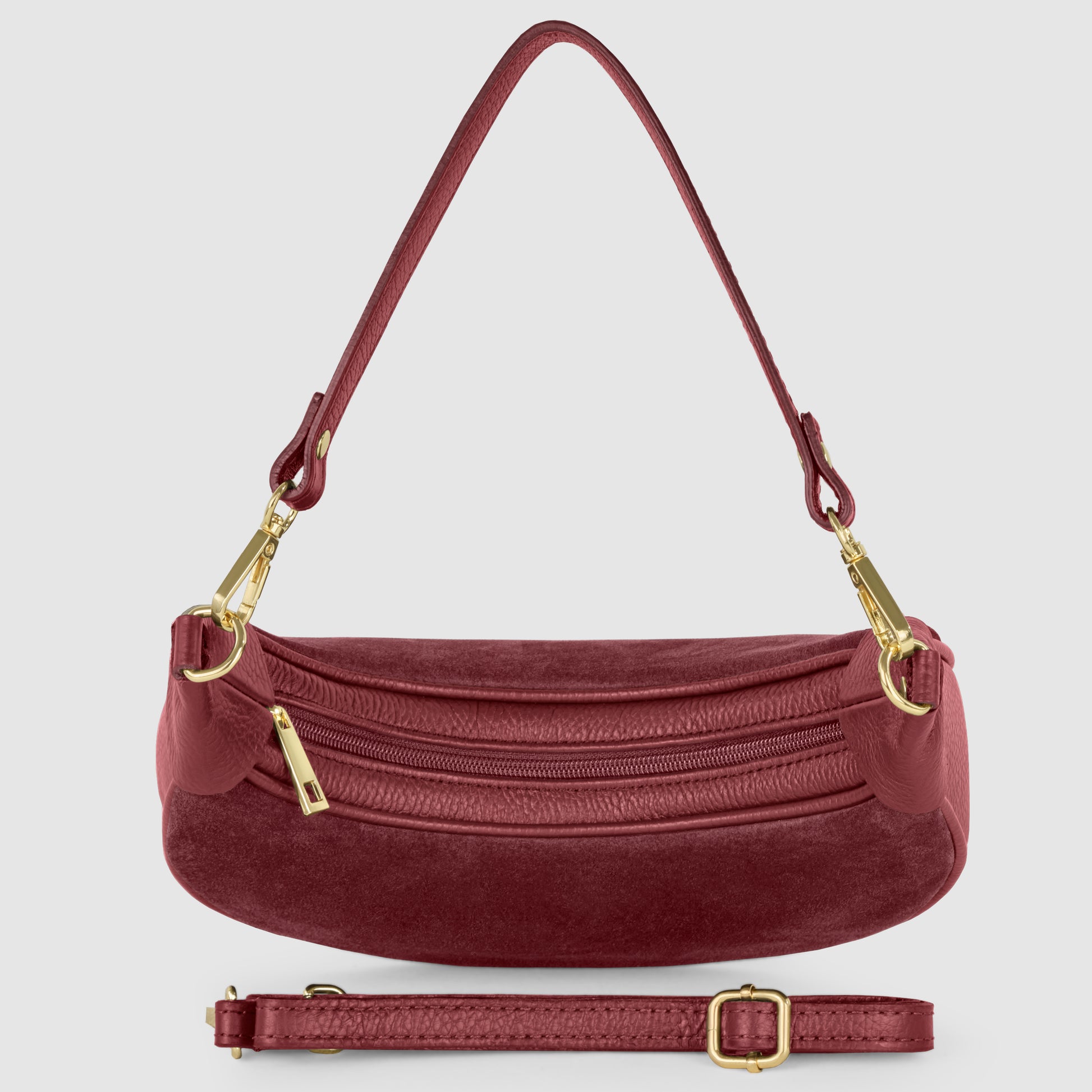 A maroon suede crescent handbag with gold hardware, a short shoulder strap, zipper closure, and an adjustable, detachable longer strap placed in front of the bag, all set against a light gray background.