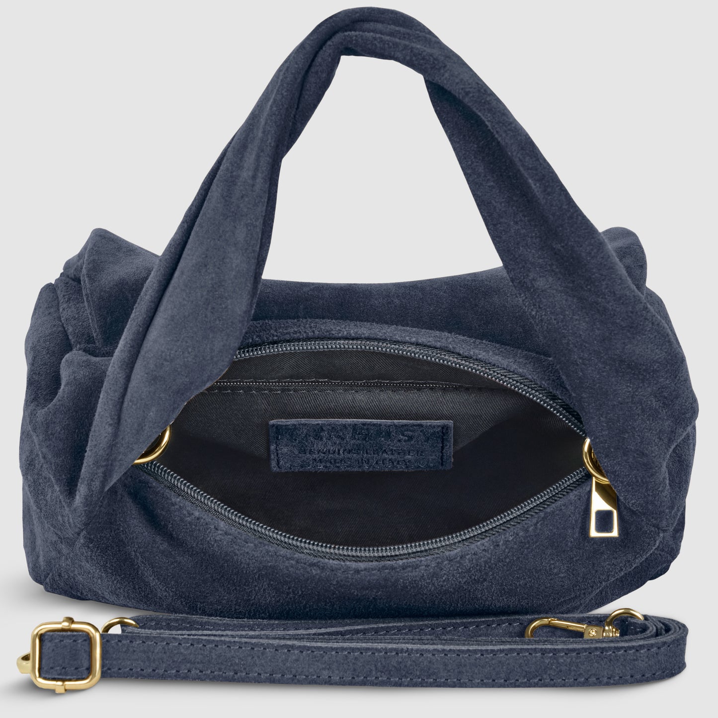 A soft, dark blue Italian suede bag with a zippered opening, gold hardware, and an adjustable shoulder strap lying in front. Handmade in Italy, this crossbody bag reveals its spacious interior.