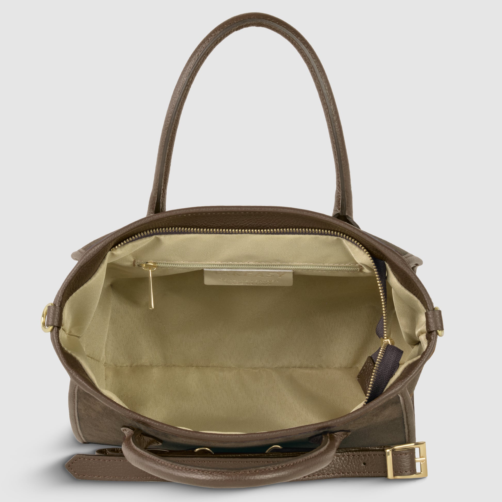 A brown suede leather handbag with gold hardware is shown open, revealing a spacious beige interior with a side pocket, zipper pull, and a small leather tag. Handcrafted in Florence, it features an adjustable detachable strap for versatile styling.