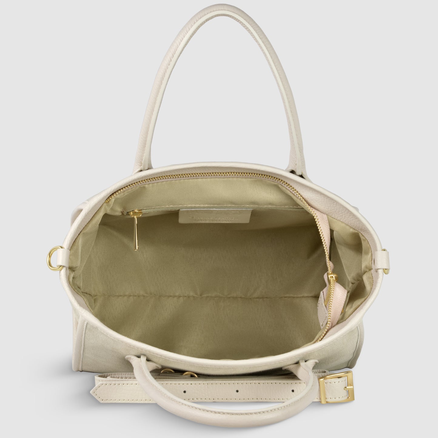 A top-down view of an open beige suede leather handbag with gold hardware, showing its spacious interior, a zippered side pocket, and an adjustable crossbody strap attached to the bag.