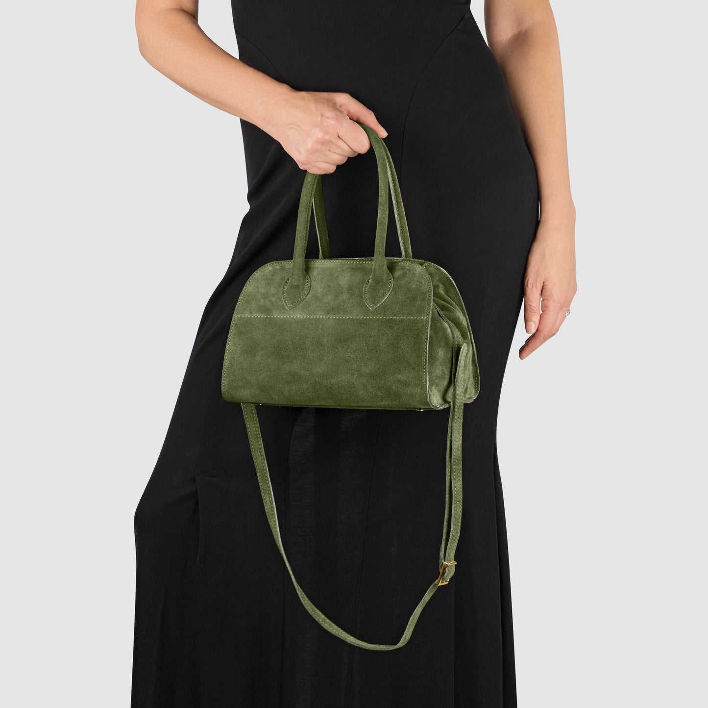 A person in a black dress holds an Italian suede handbag, handmade in Italy by Florentine leather artisans, featuring double handles and a shoulder strap against a plain light background.
