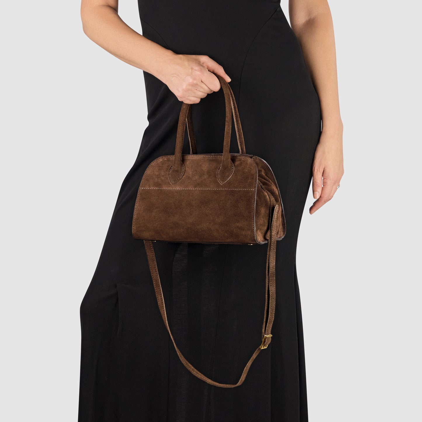A person in a black dress holds a Handmade Italian handbag crafted from genuine suede, featuring both short handles and a long shoulder strap, against a light gray background.
