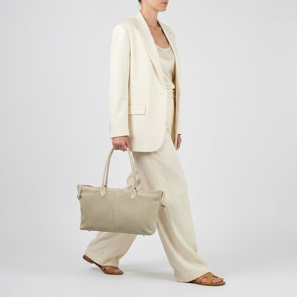A person in a cream-colored suit and sandals walks while carrying an Italian suede tote bag, made in Italy, with two handles against a plain white background.