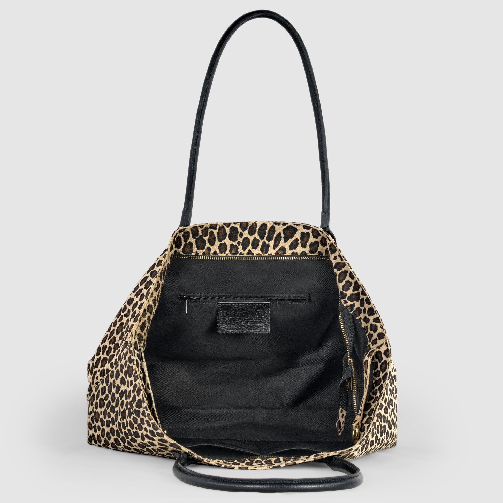 A leopard print Italian-crafted tote with black interior, shown open to reveal a zippered pocket and label inside. The bag has two black handles and is displayed against a light gray background.
