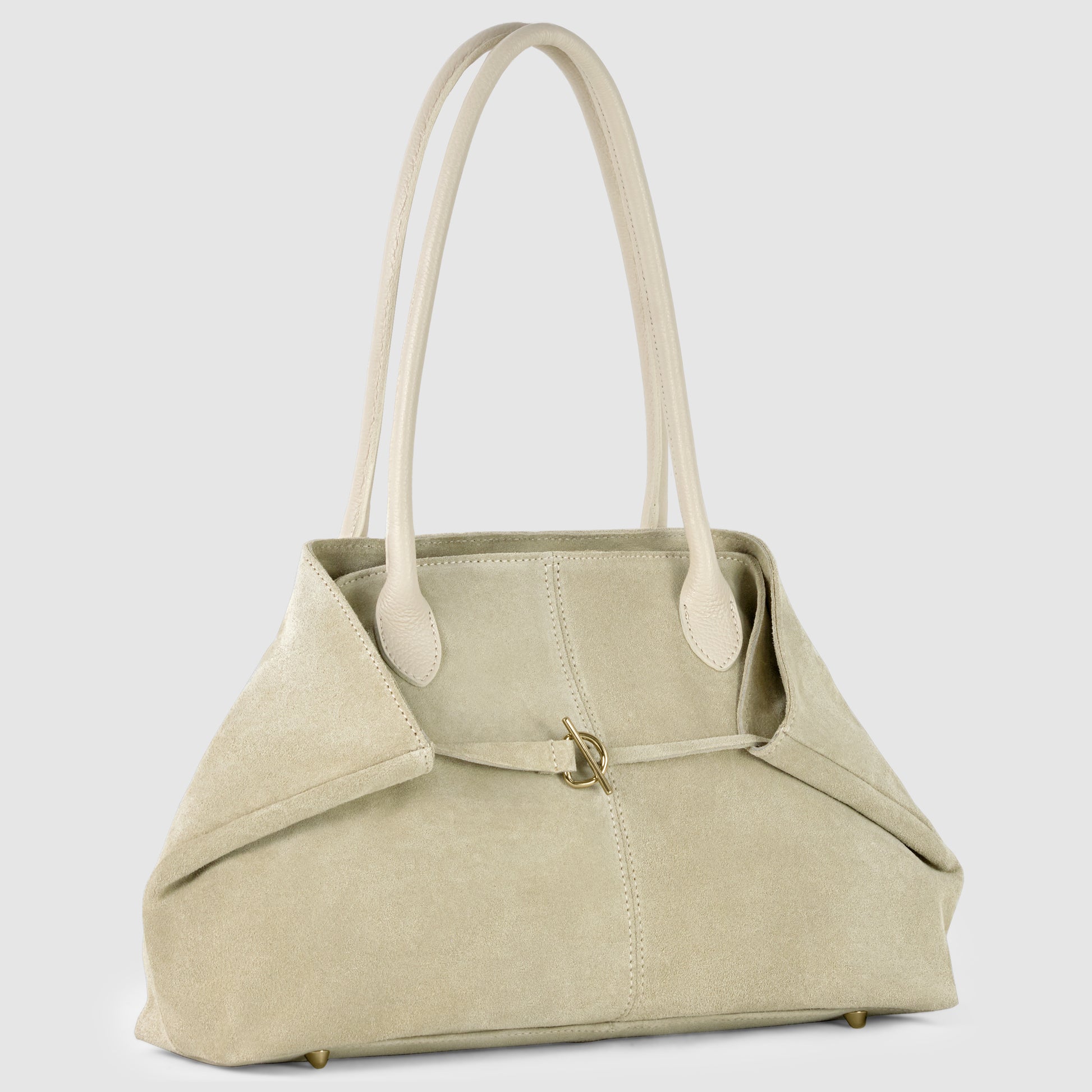 A beige Italian-crafted tote with long, light leather handles, a soft suede structure, gold-tone hardware, and a central buckle detail stands upright against a light gray background.