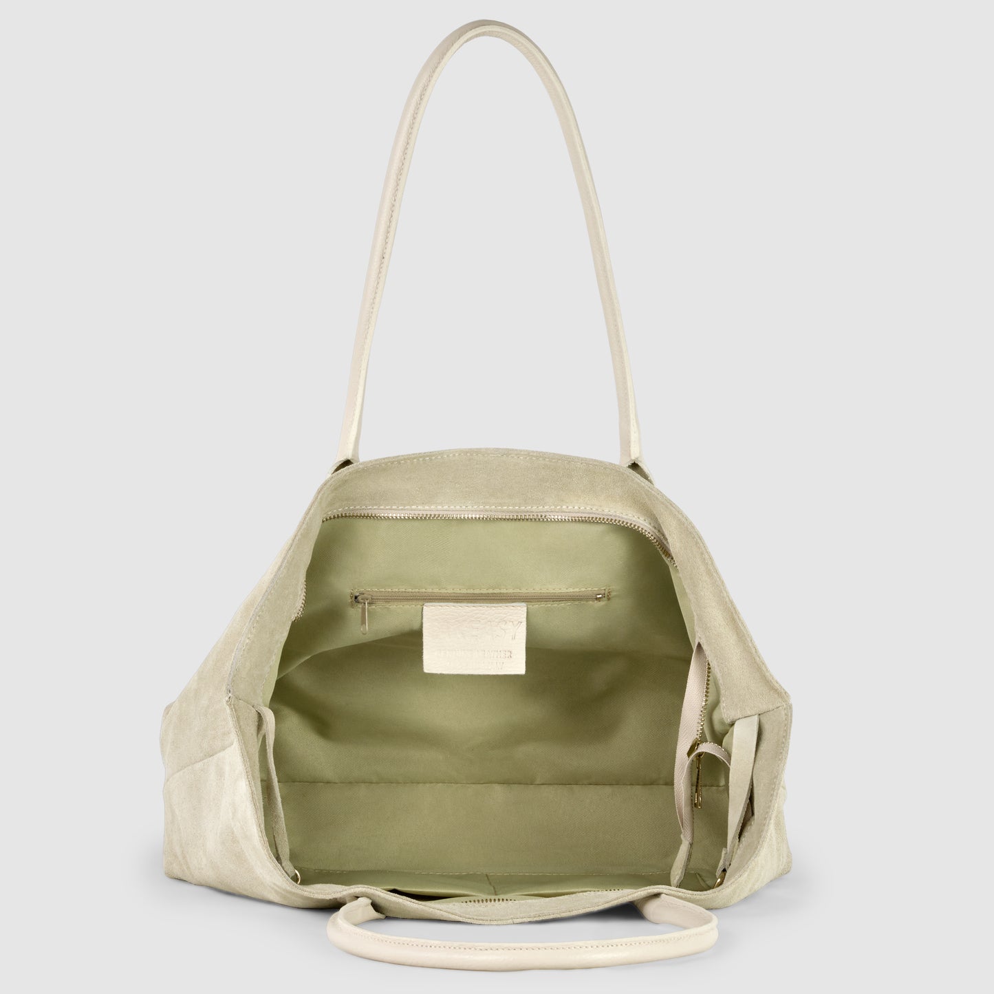 A light beige Italian-crafted tote is shown open, revealing a spacious interior lined with light green fabric, an inner zippered pocket, and a small white label sewn inside.