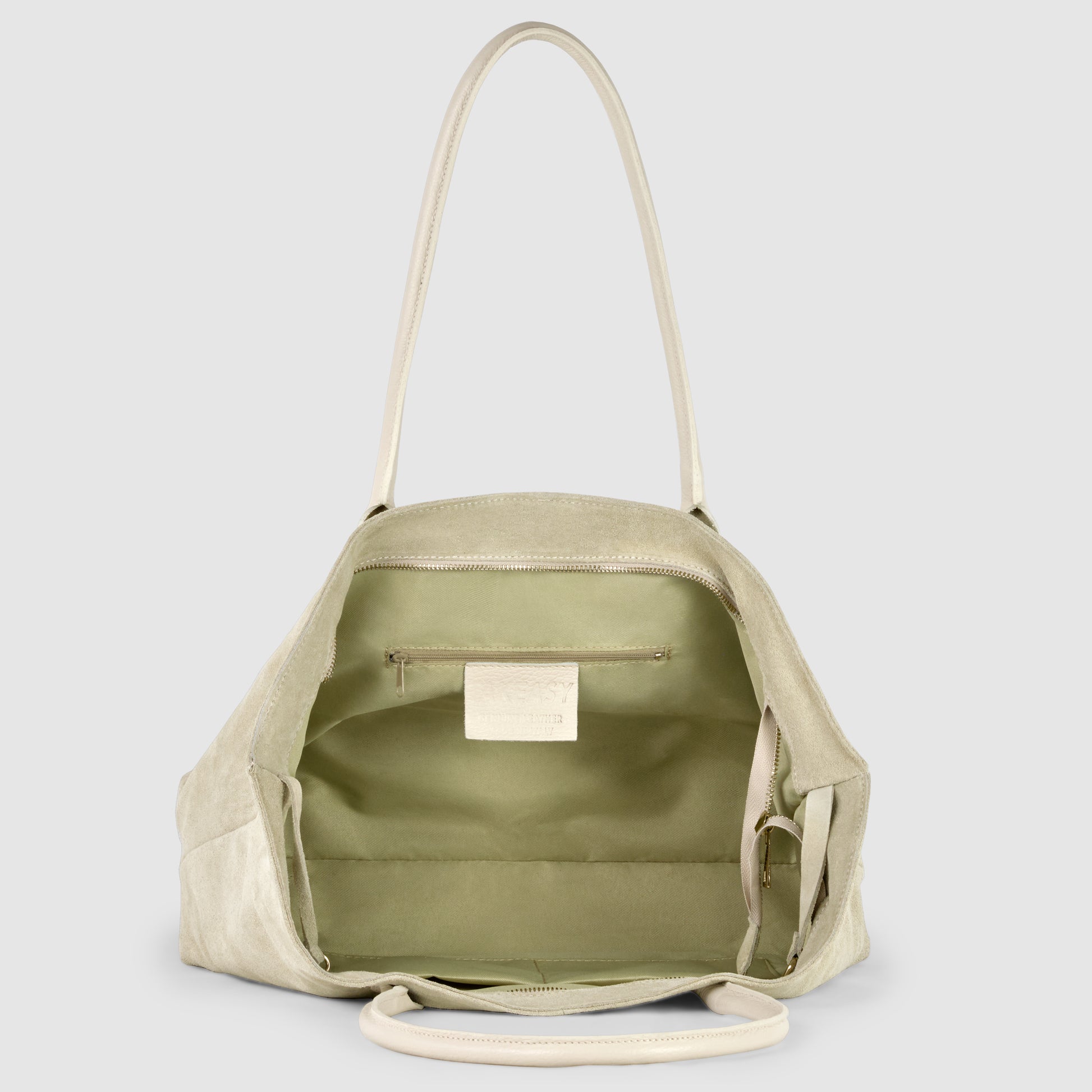 A light beige Italian-crafted tote is shown open, revealing a spacious interior lined with light green fabric, an inner zippered pocket, and a small white label sewn inside.