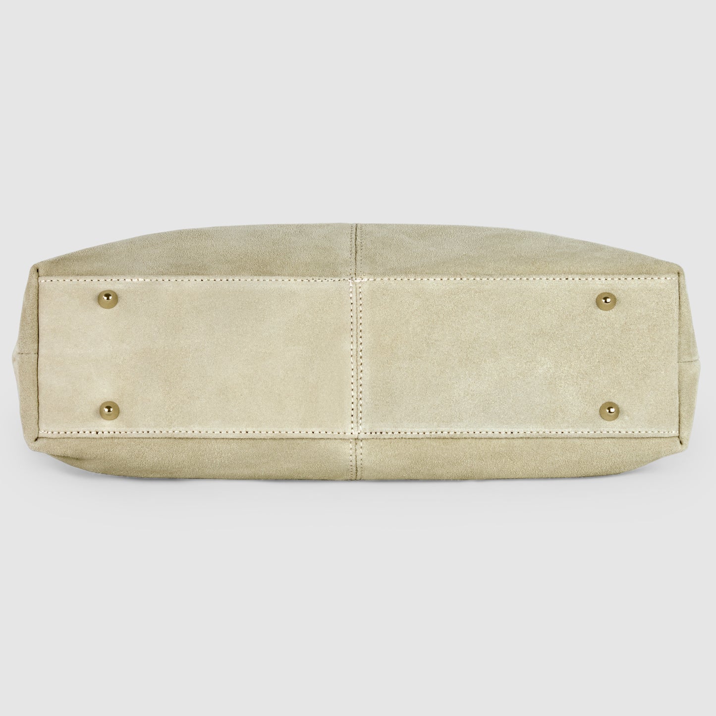 The image shows the bottom view of a beige suede tote bag with four gold metal studs and visible stitching along the seams.