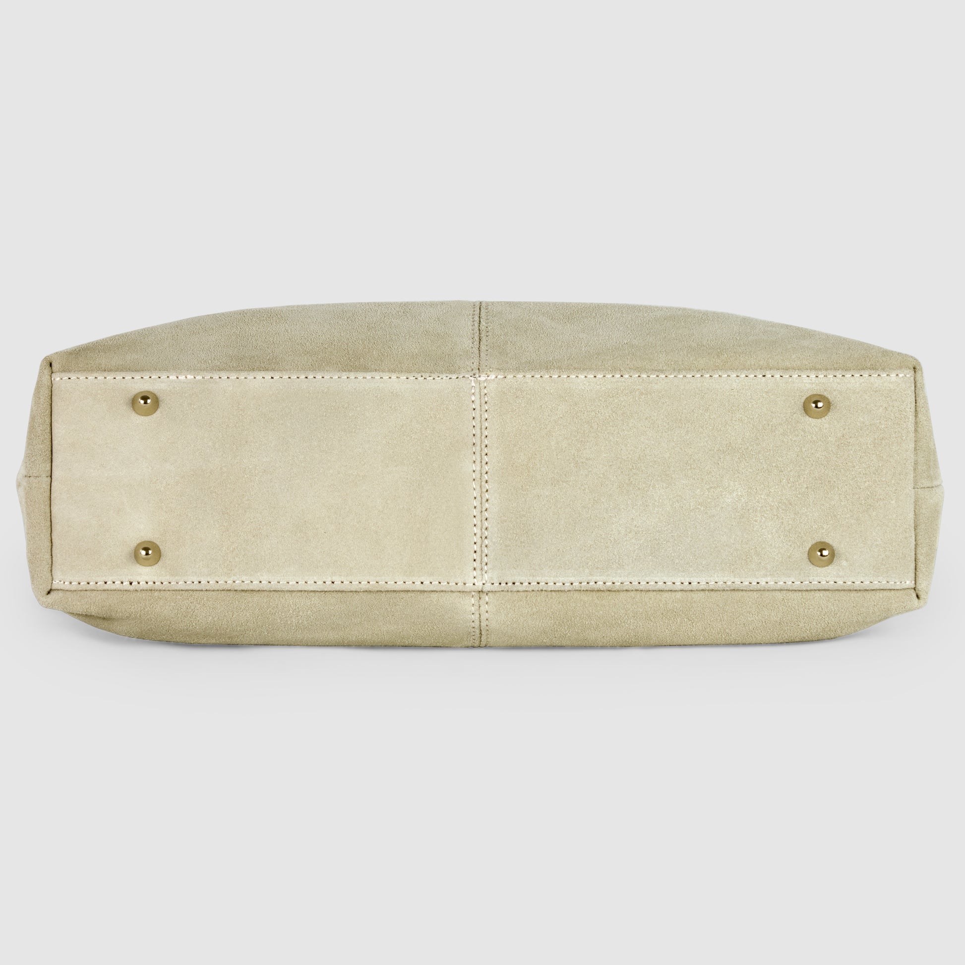 The image shows the bottom view of a beige suede tote bag with four gold metal studs and visible stitching along the seams.