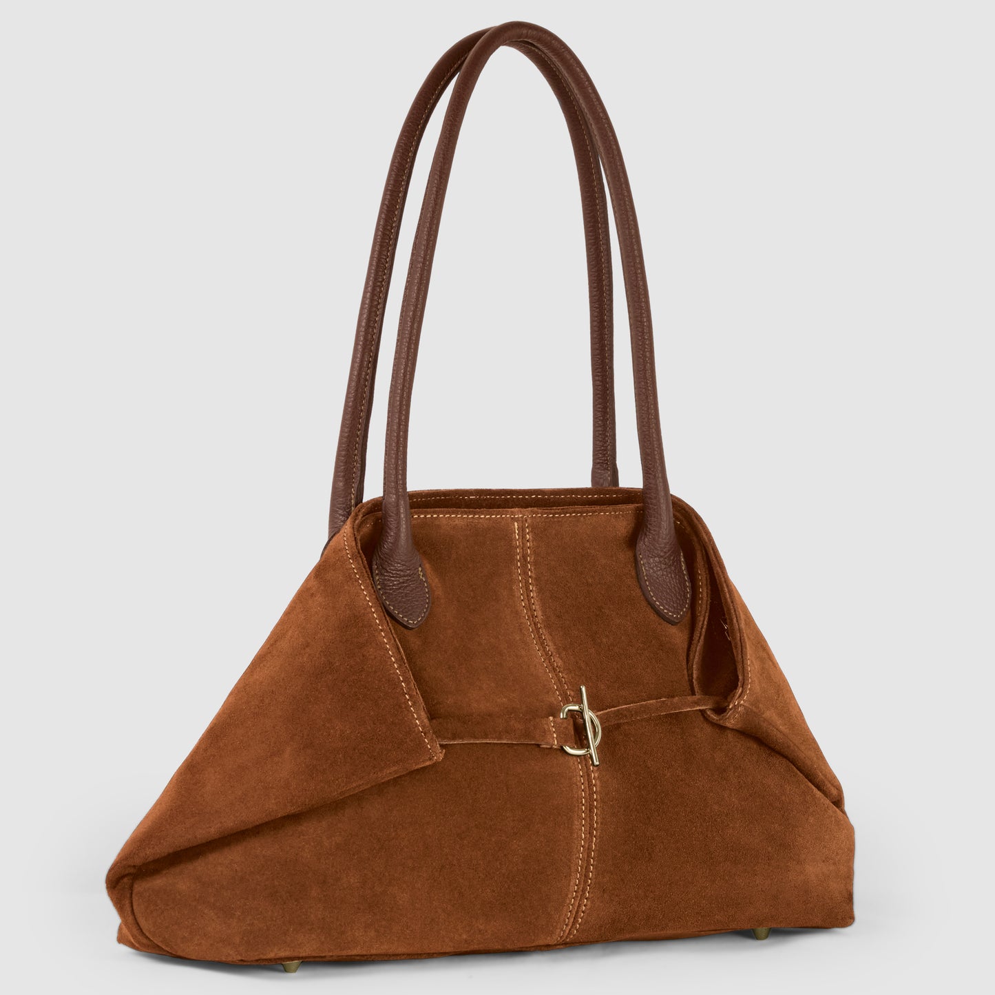 An Italian-crafted suede tote bag with long dark brown leather handles, a soft structured body, visible stitching, a small buckle detail on the front, and metal feet on the bottom, displayed against a light gray background.