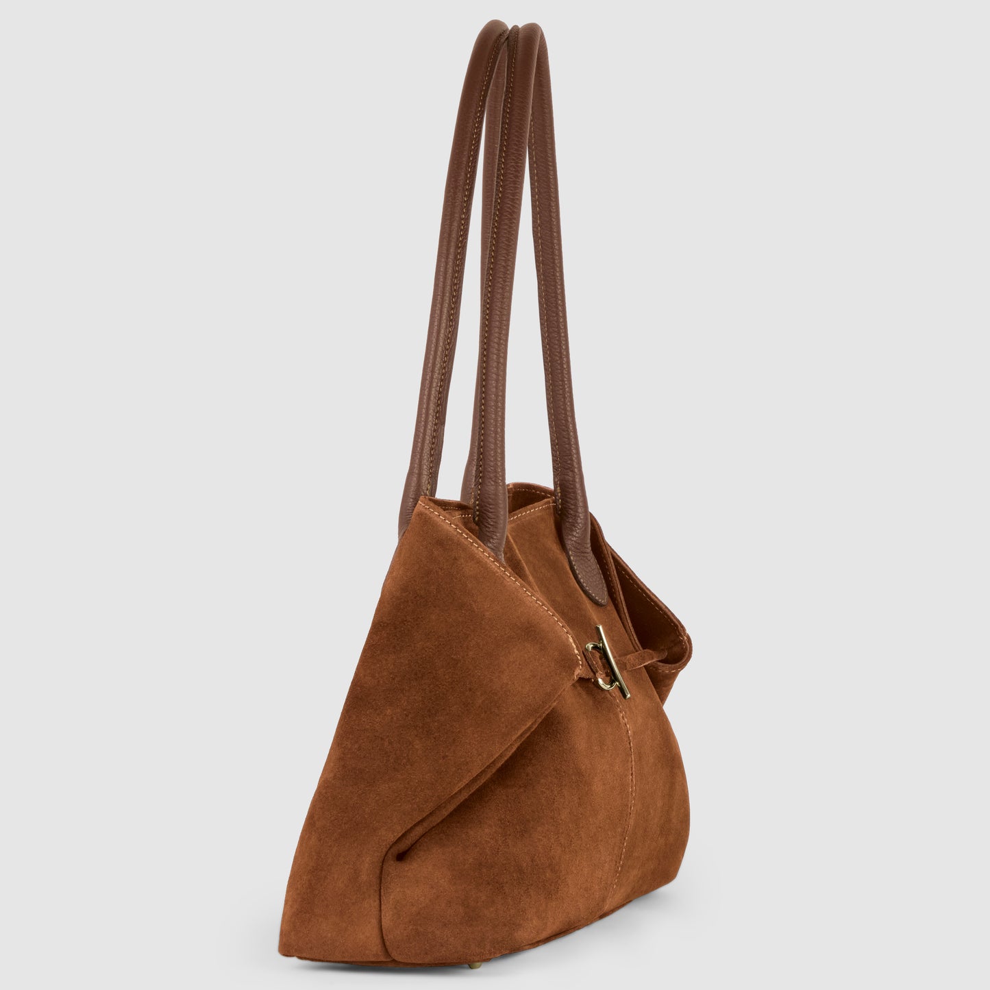 A brown suede tote bag with two long, dark brown leather handles and a gold buckle detail, displayed on a light grey background, shown from a side angle.