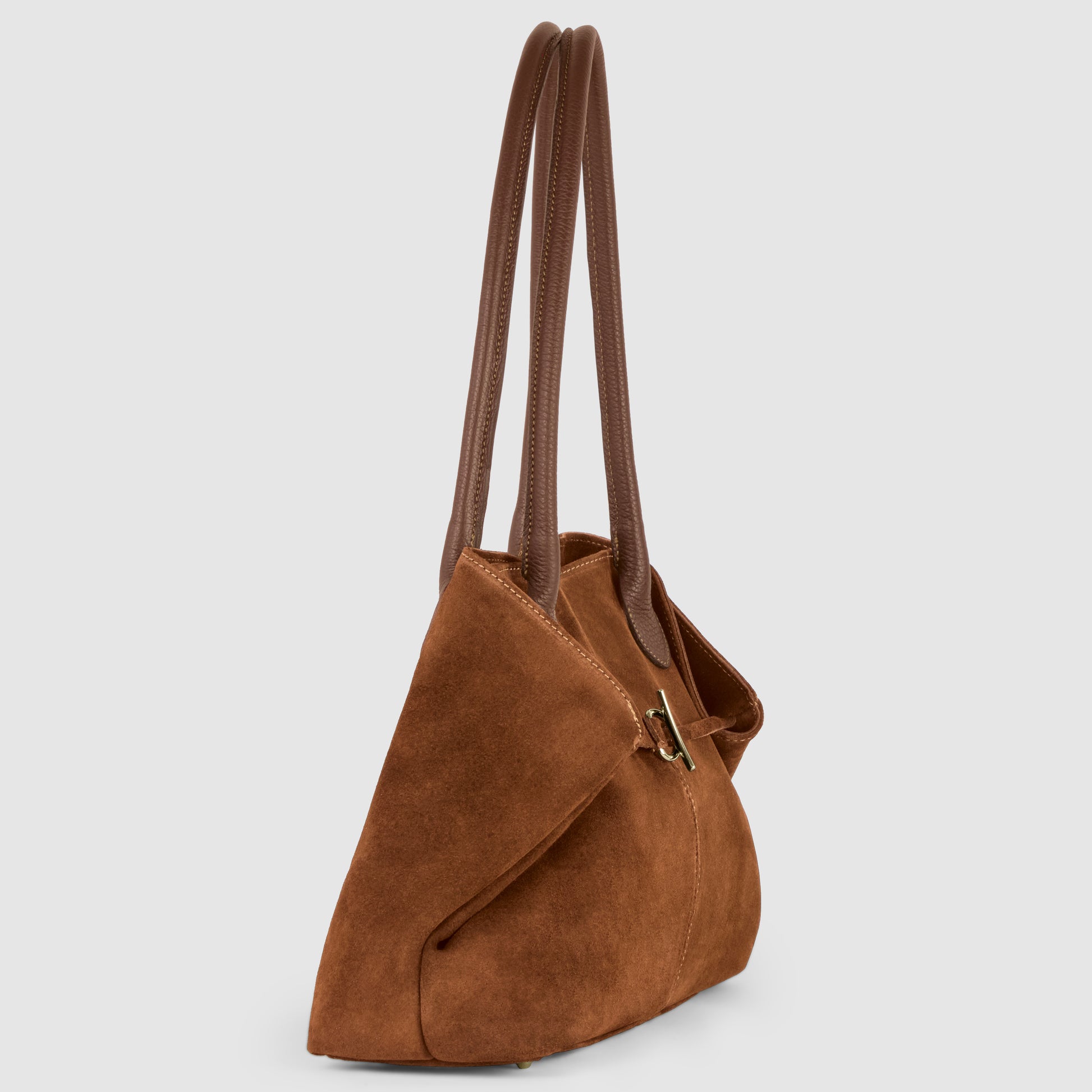 A brown suede tote bag with two long, dark brown leather handles and a gold buckle detail, displayed on a light grey background, shown from a side angle.