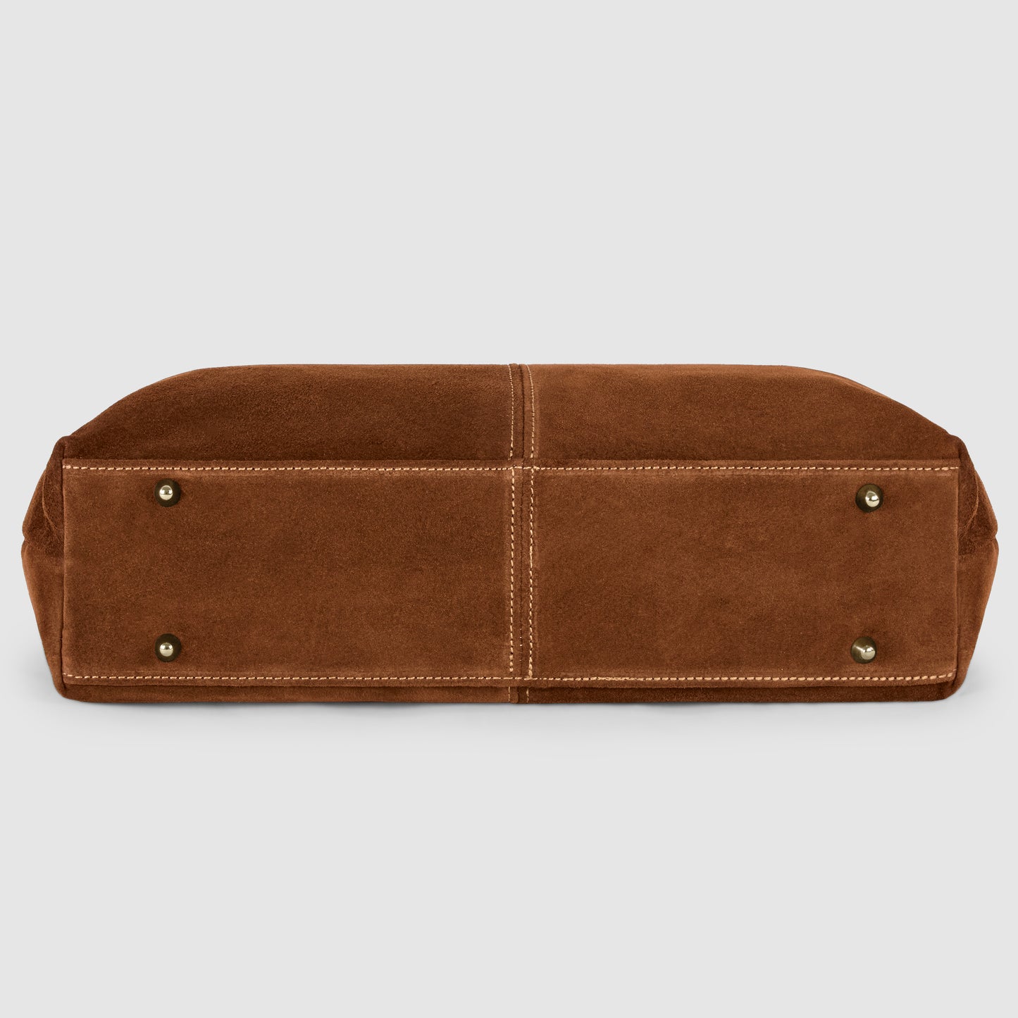 A brown suede tote bag shown from the bottom, featuring four small metal feet and visible stitching details along the seams.