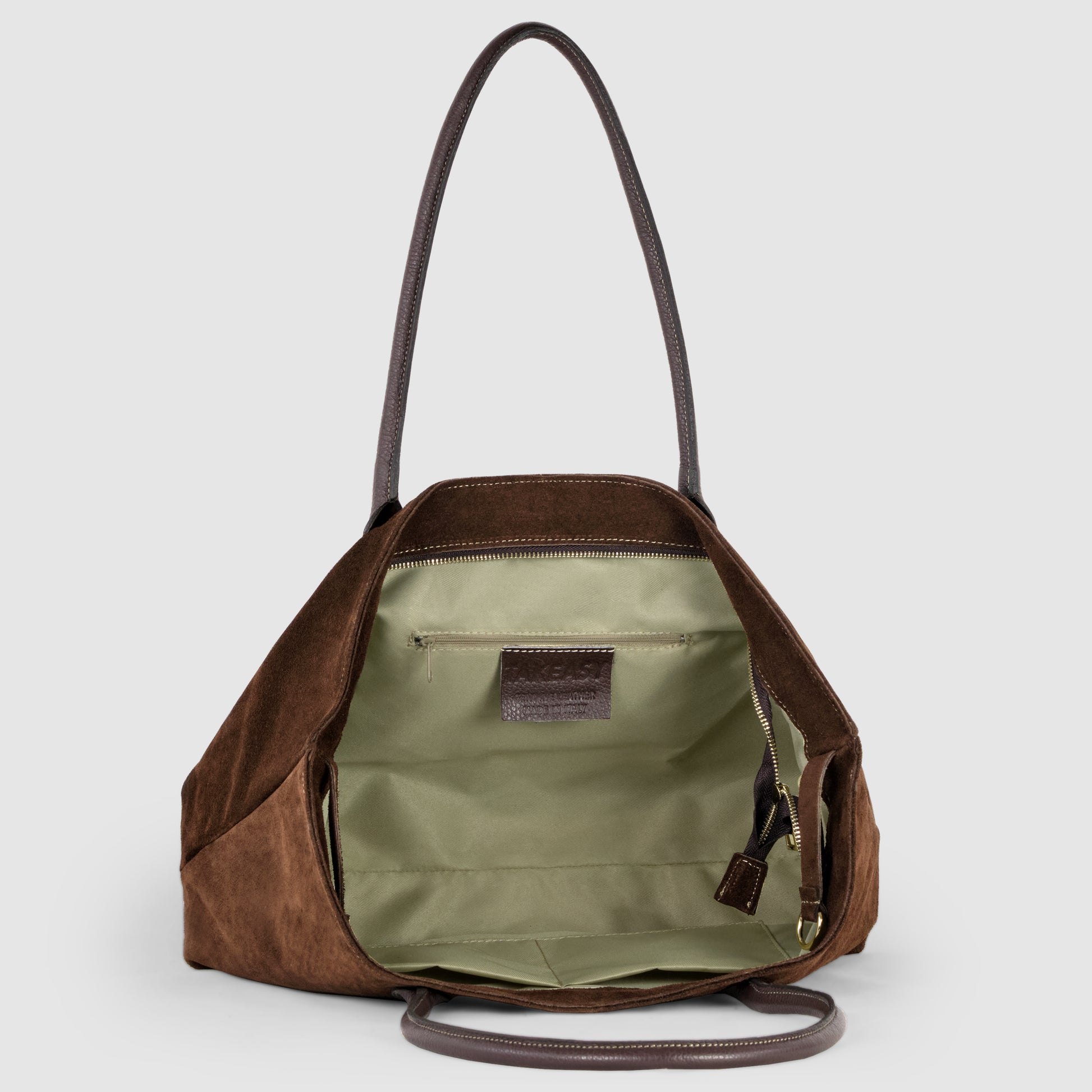 A brown Italian suede tote bag with dark handles shown open, revealing a spacious light green interior, an inner zip pocket, and a leather logo patch. Perfect as a stylish women’s tote.